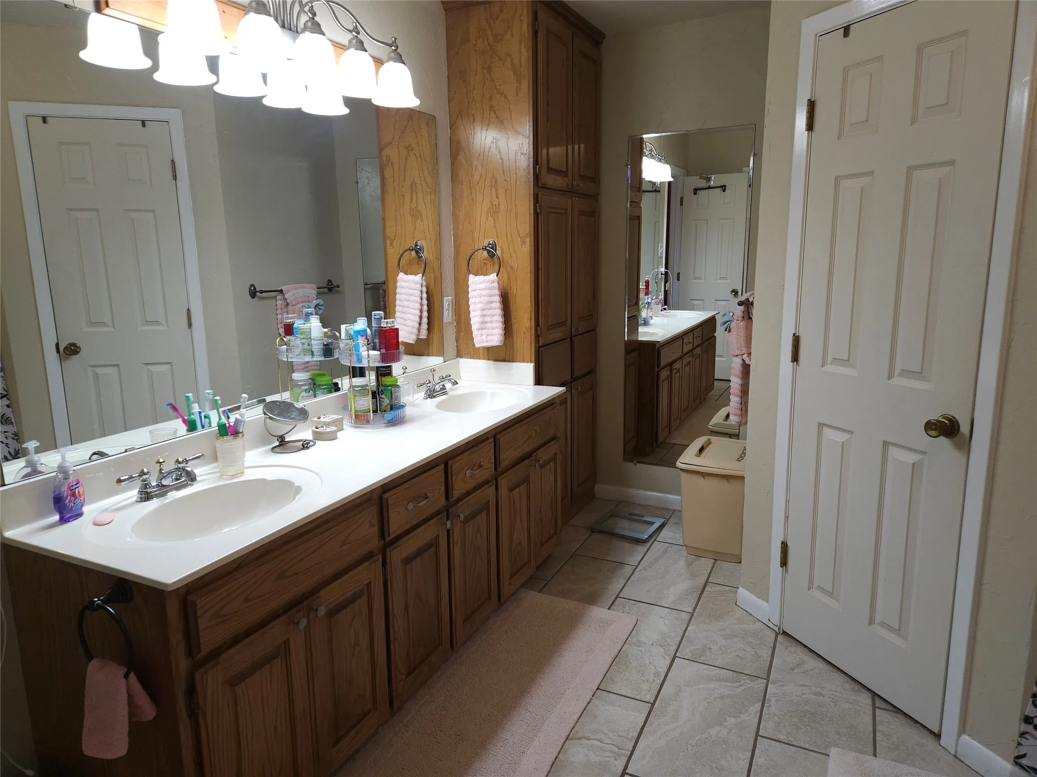 Double vanity with undermount sinks, wood cabinetry, large vanity mirror, built-in storage cabinet, his and hers walk-in closets