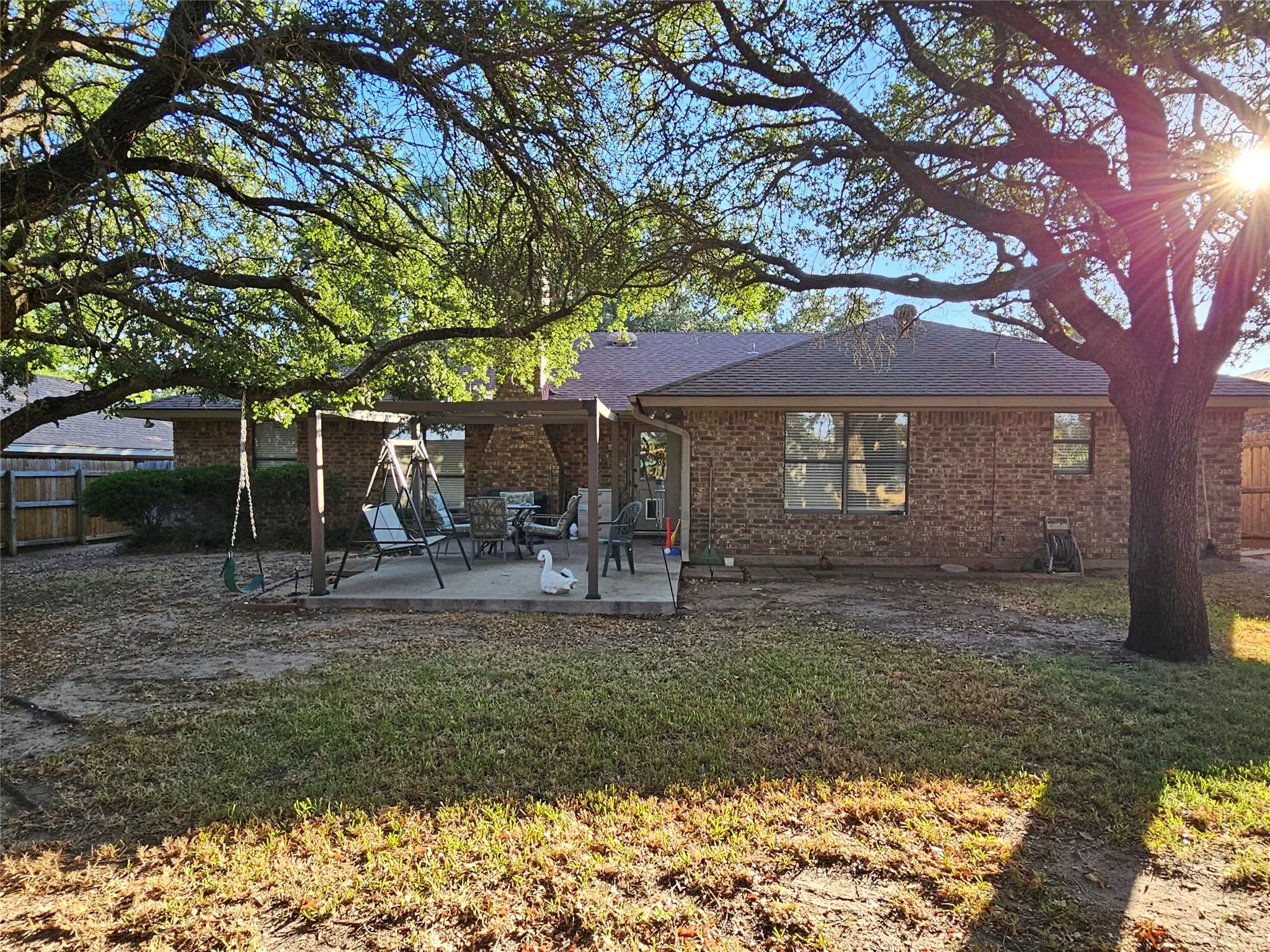 Brick exterior home with a partial privacy fence and an expansive concrete patio featuring a pergola