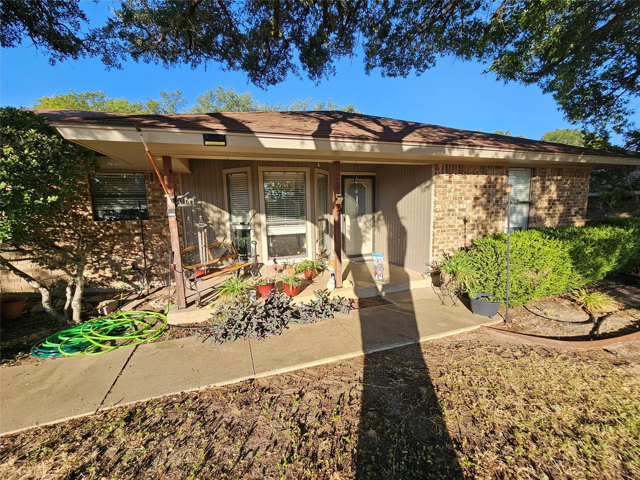 Exterior featuring brick and vertical siding, a covered entryway, and mature landscaping