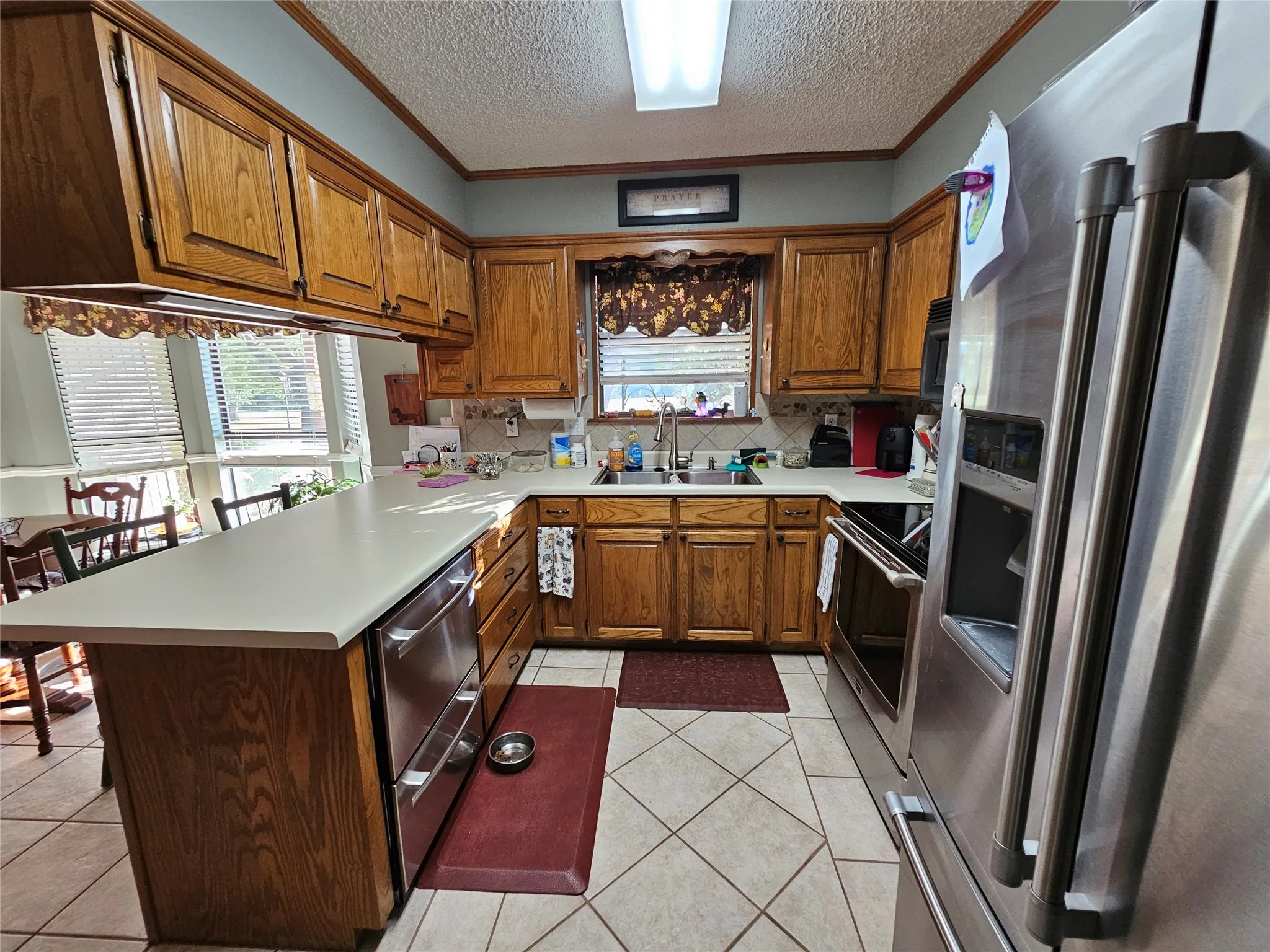 U-shaped kitchen with wood cabinetry, light-colored countertops, and stainless steel appliances