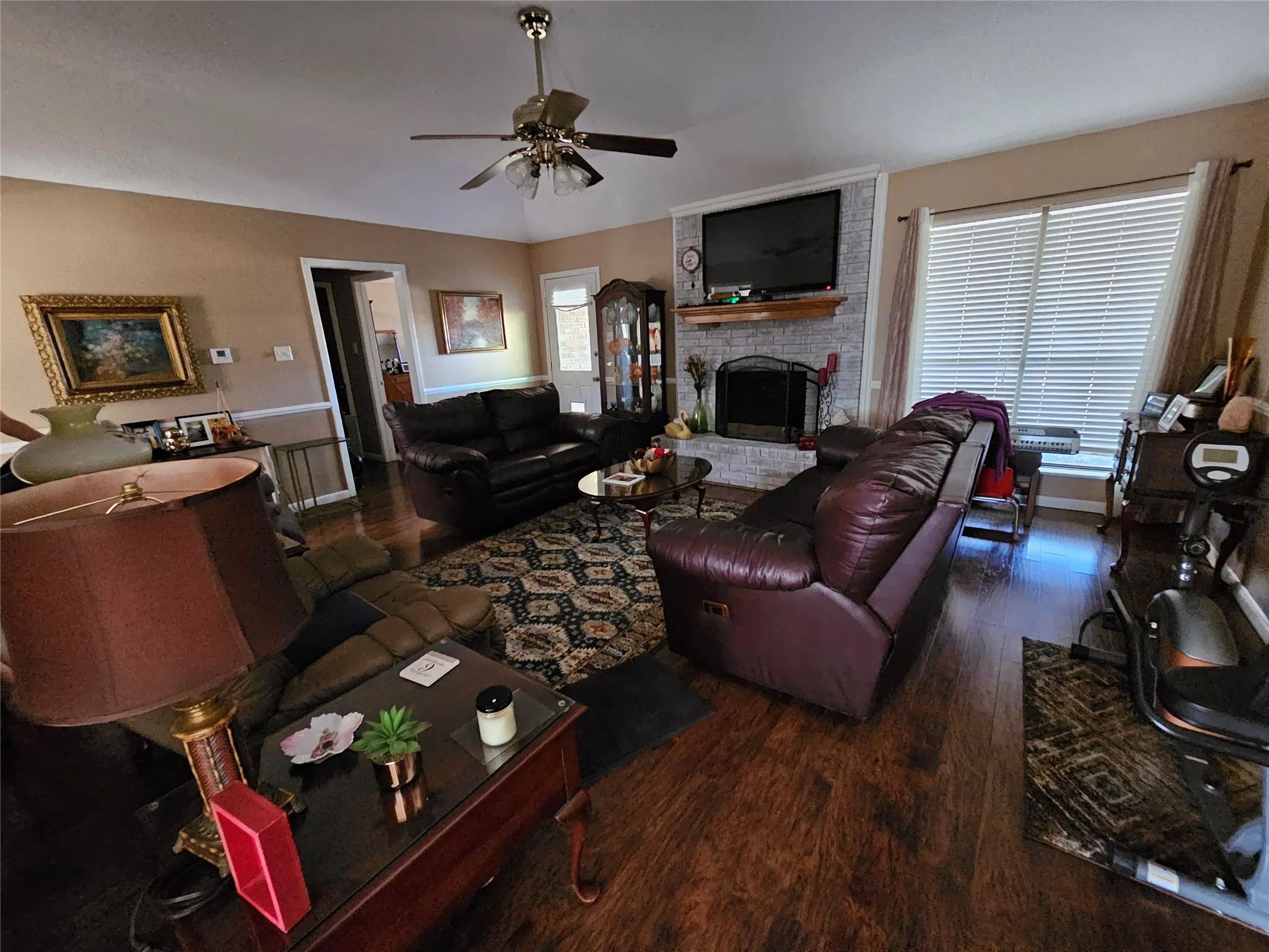 Wood-finish flooring, ceiling fan, and a fireplace with a stone-clad surround and wood mantel