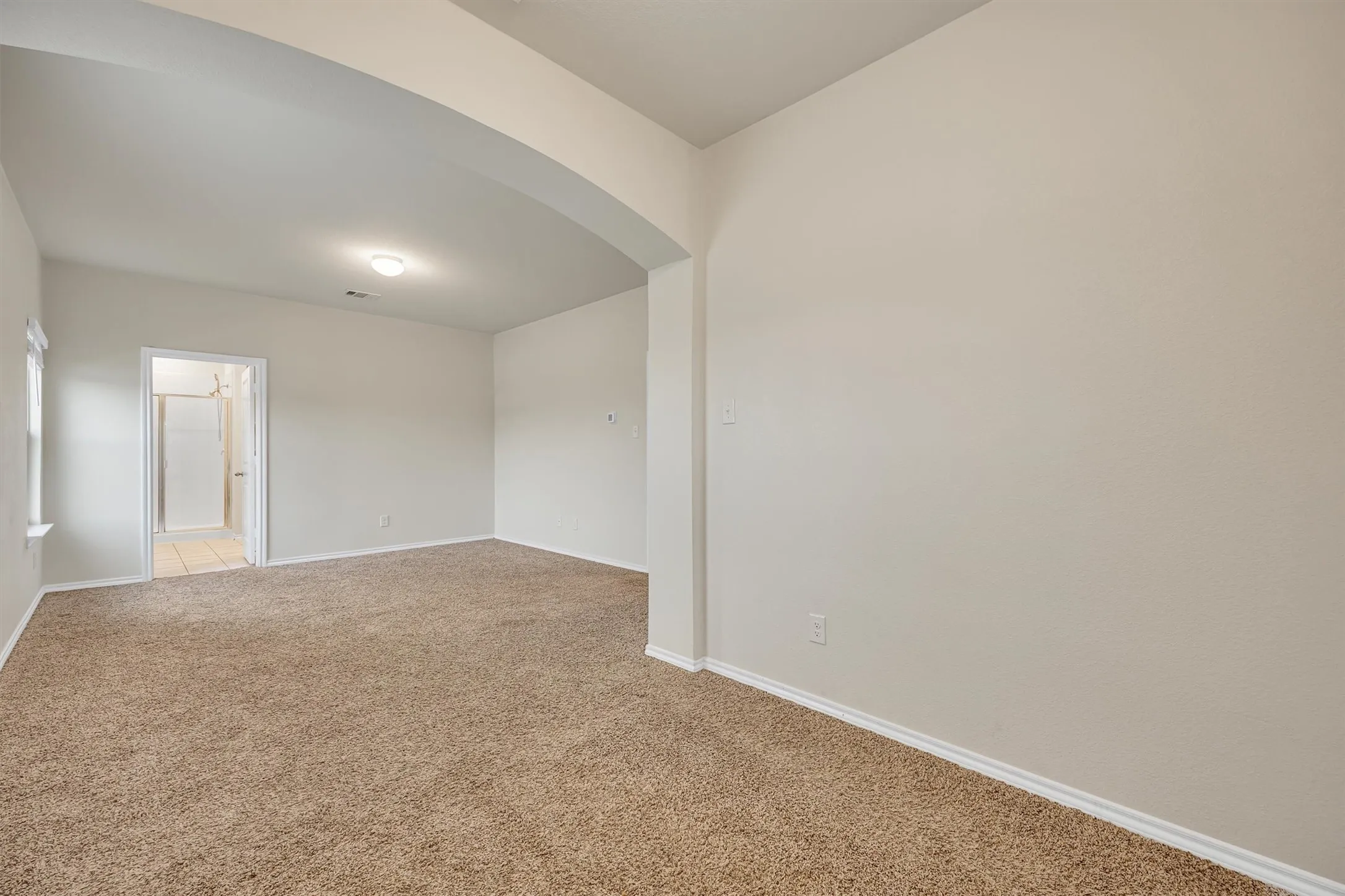 Arched entryway to a carpeted room featuring a single window, overhead lighting, and neutral wall paint