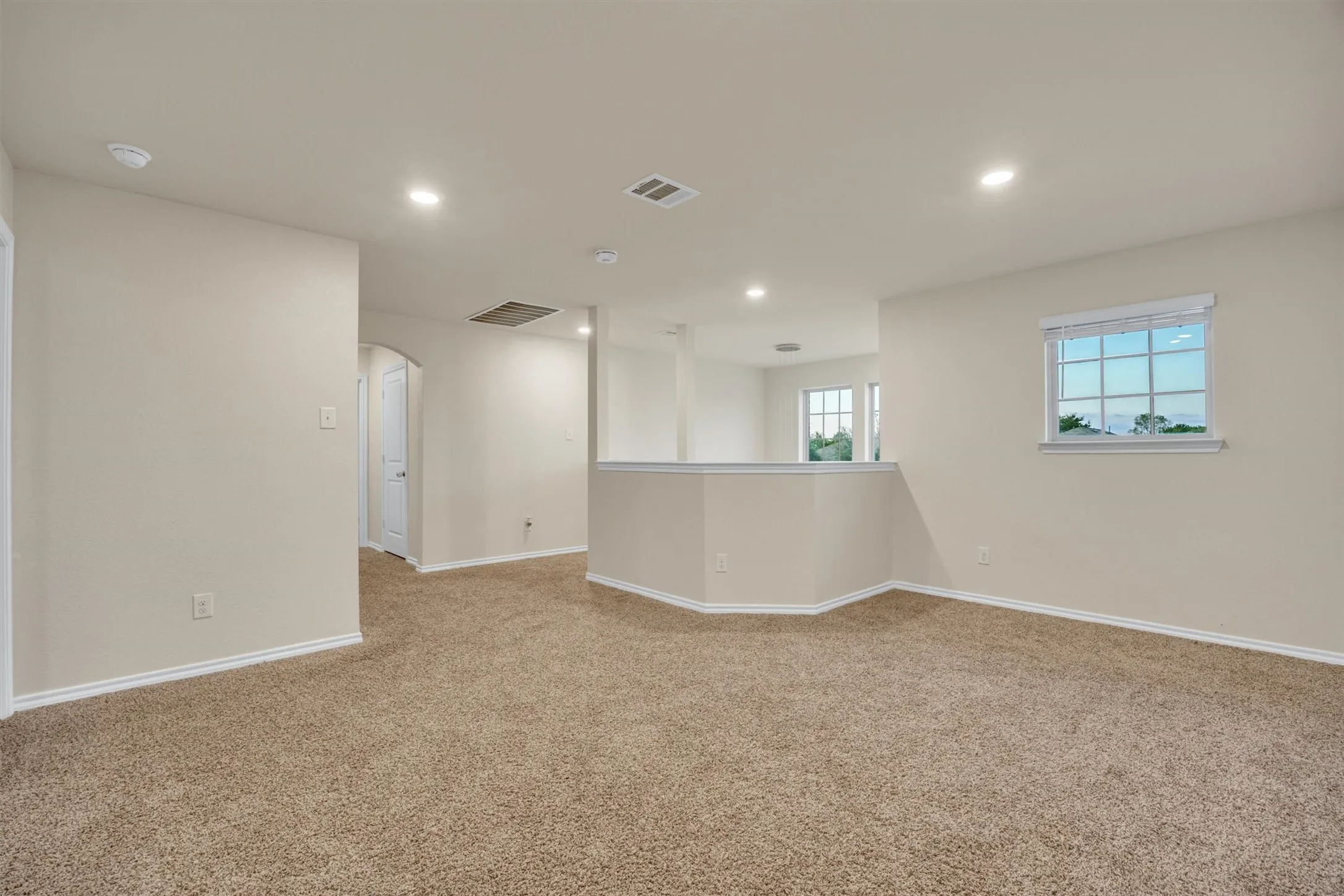 Spacious carpeted area featuring recessed lighting, a window with blinds, and a built-in half-wall partition