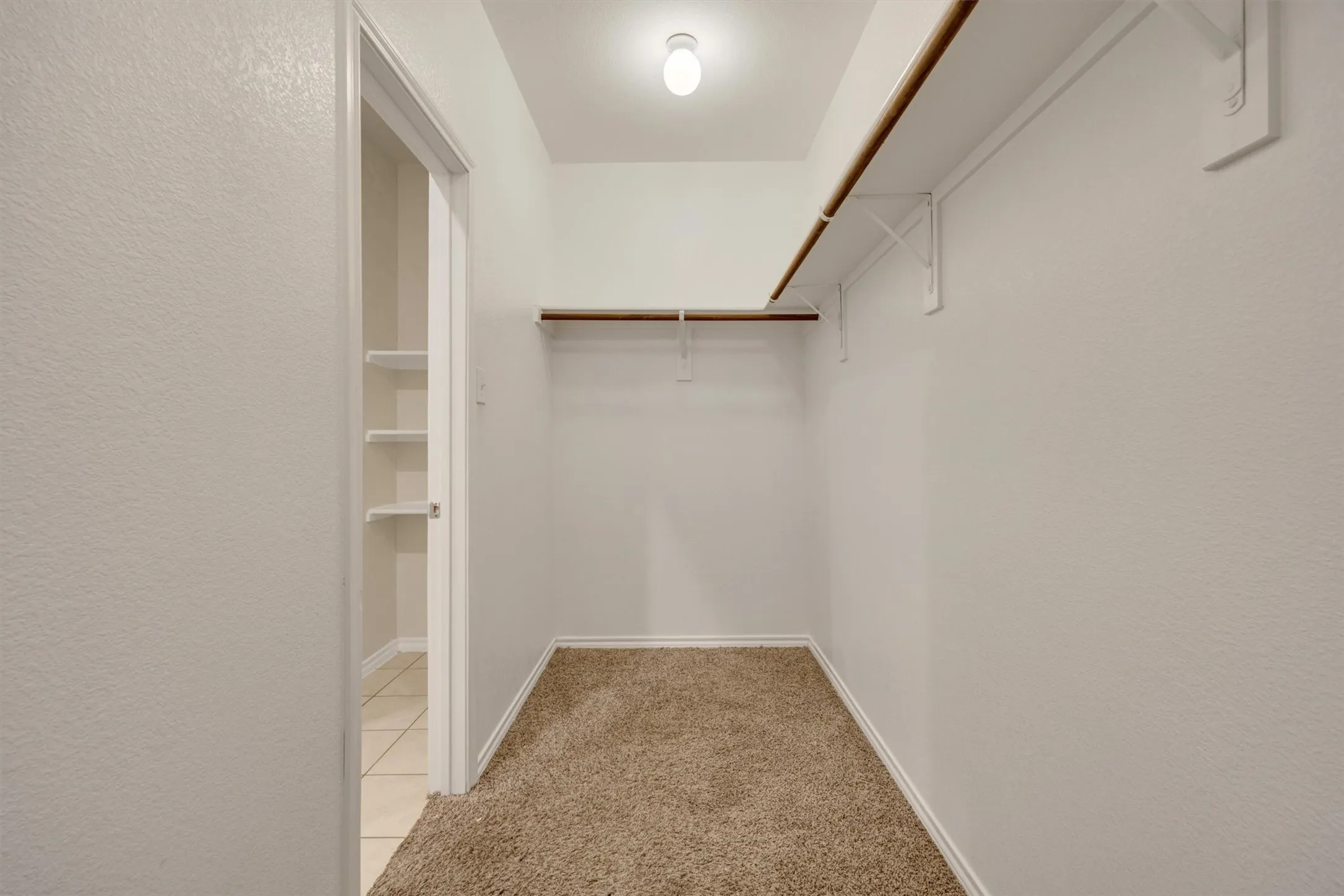 Recessed lighting, wall-mounted shelving, wood-finish hanging rods, and carpet flooring