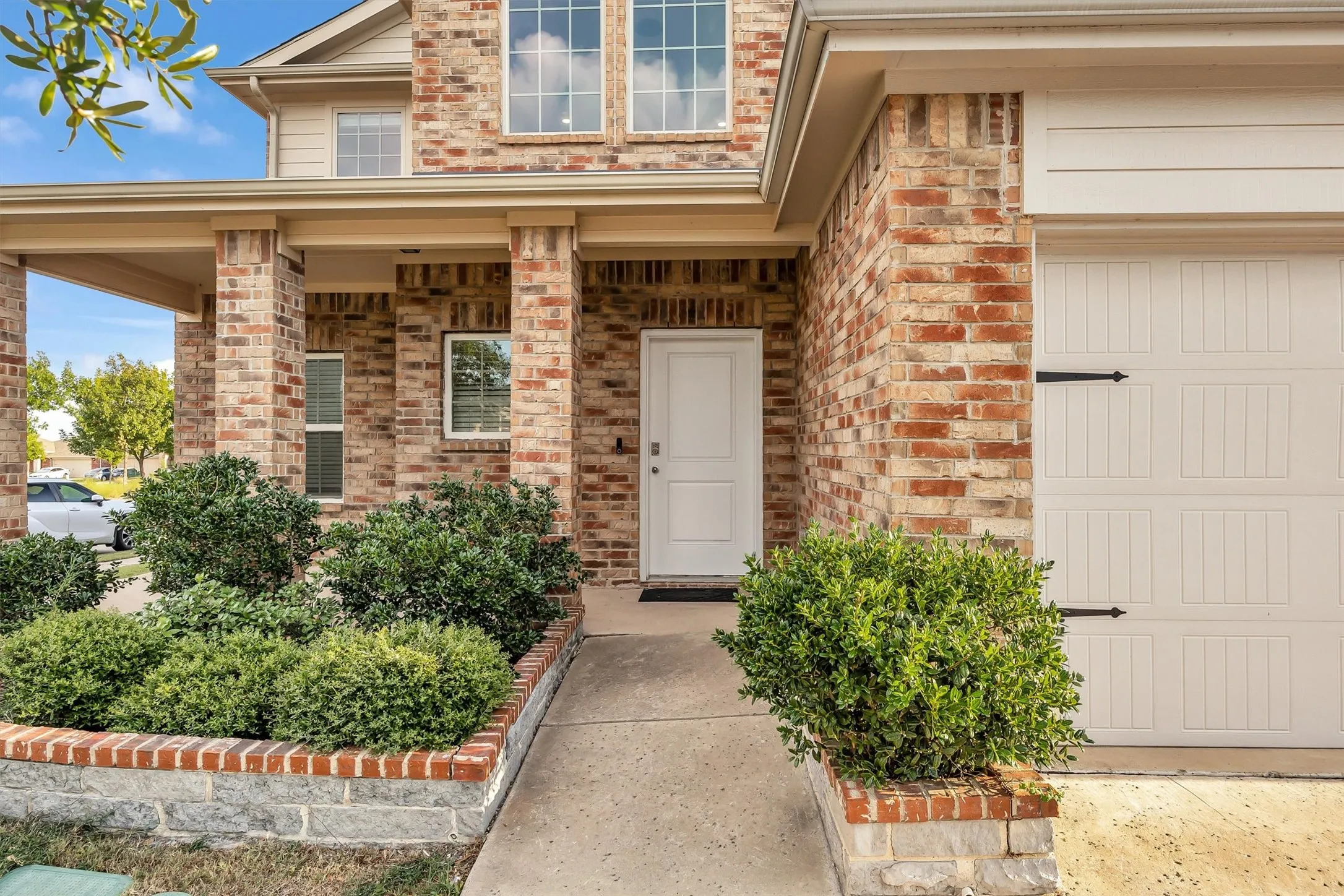 Brick exterior with an integrated garage, covered entry, and decorative shrubbery