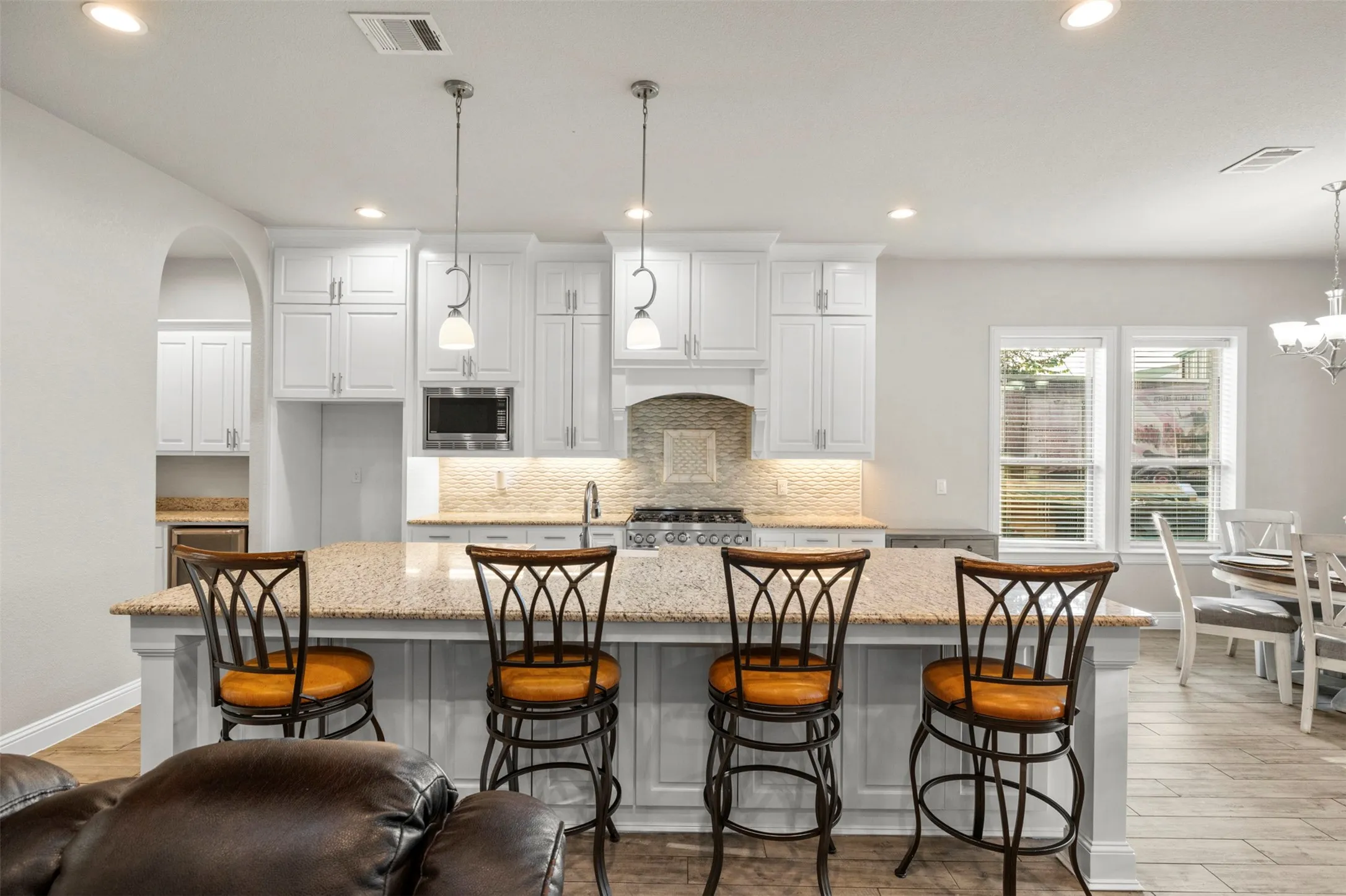 White shaker-style cabinetry, a spacious kitchen island with a granite countertop, stainless steel appliances, and a tiled backsplash