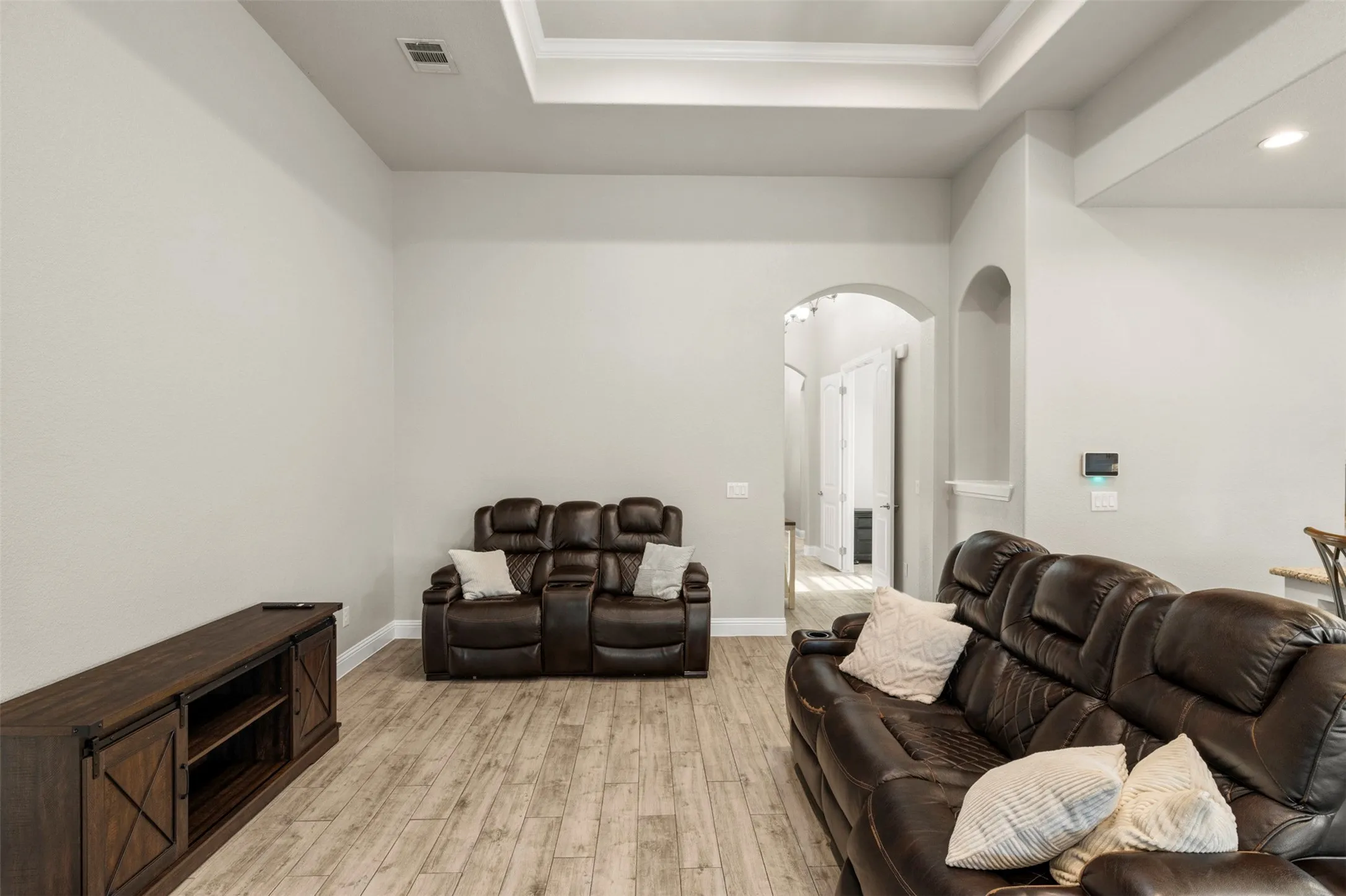 Tray ceiling, recessed lighting, wood-finish flooring, light-toned walls, arched doorway
