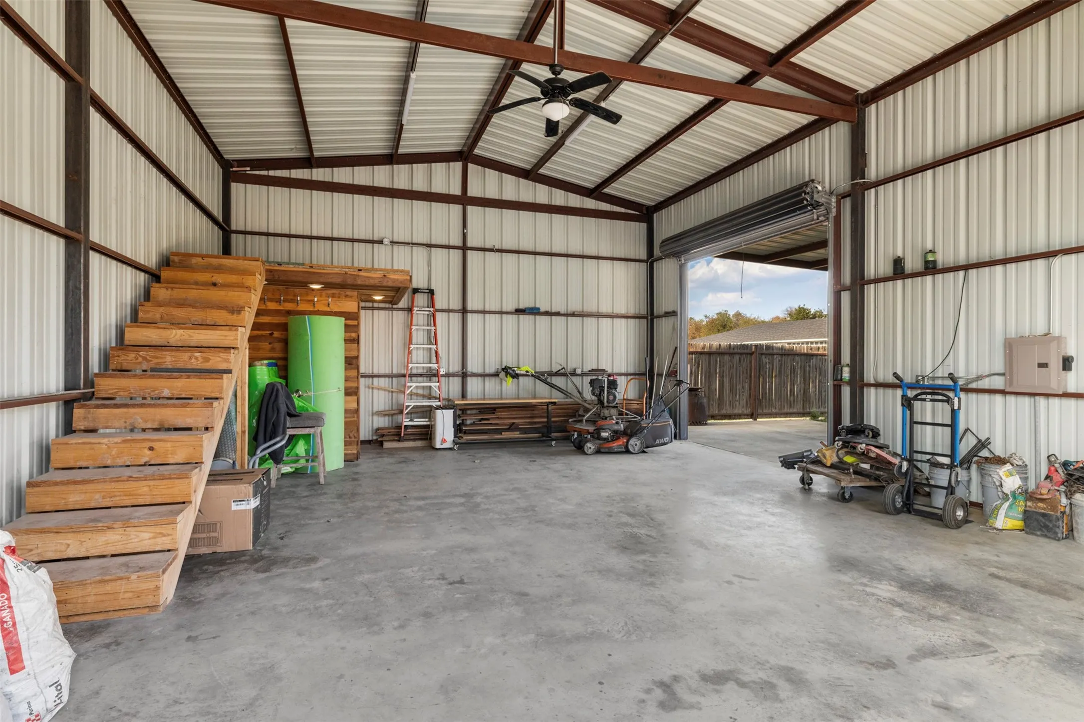 Metal-frame structure with corrugated metal walls and ceiling, exposed beam ceiling, concrete flooring, and a ceiling fan