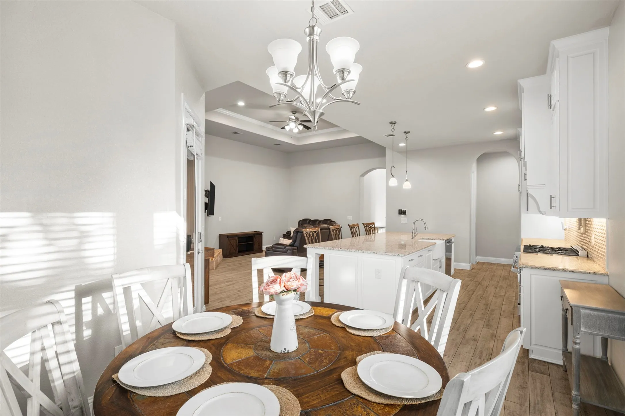Open-concept living space featuring a kitchen with white cabinetry, a center island with a sink, and a gas cooktop with a tile backsplash