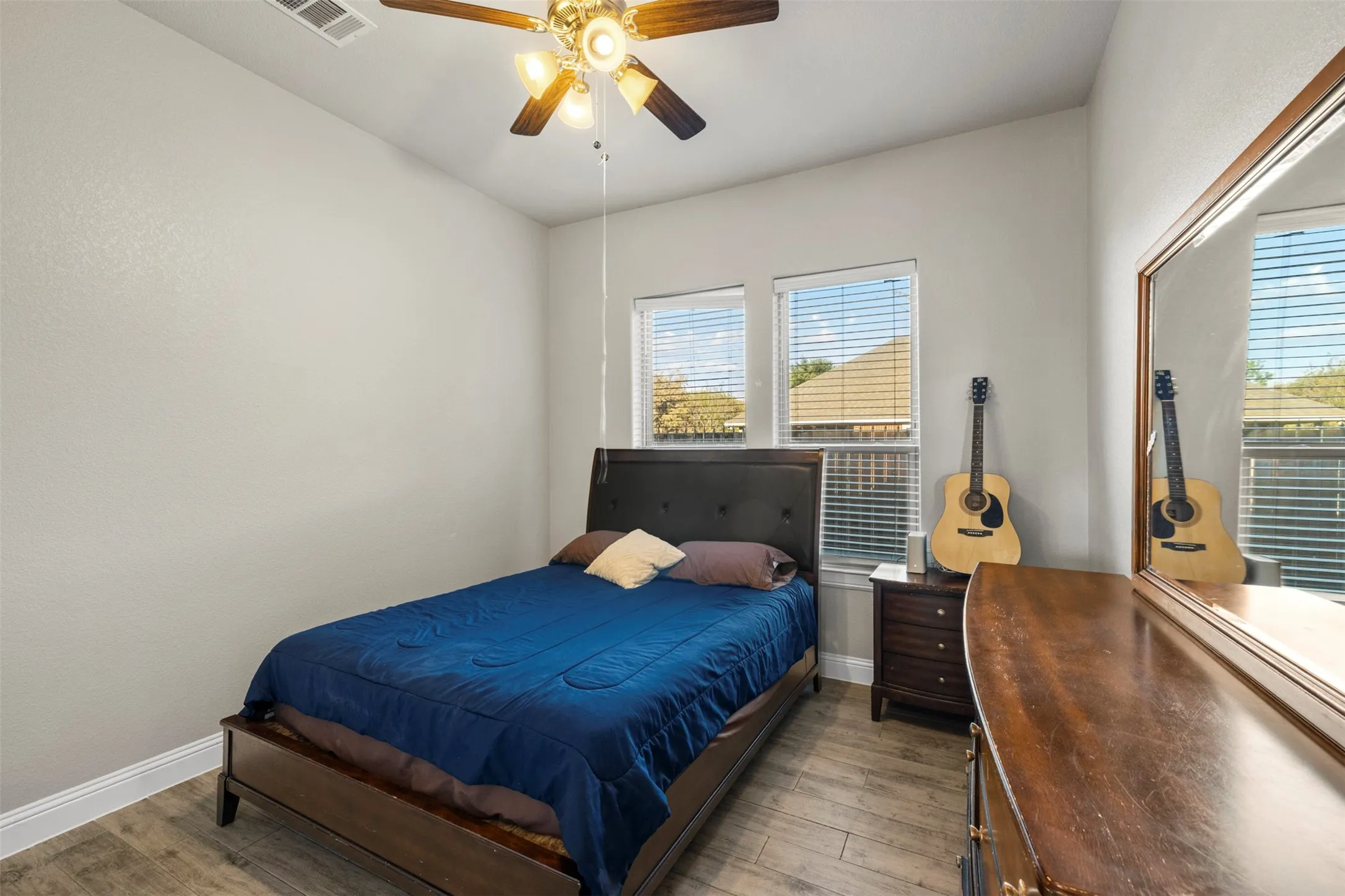 Wood-finish flooring, two windows with blinds, ceiling fan with integrated lighting, and neutral wall paint