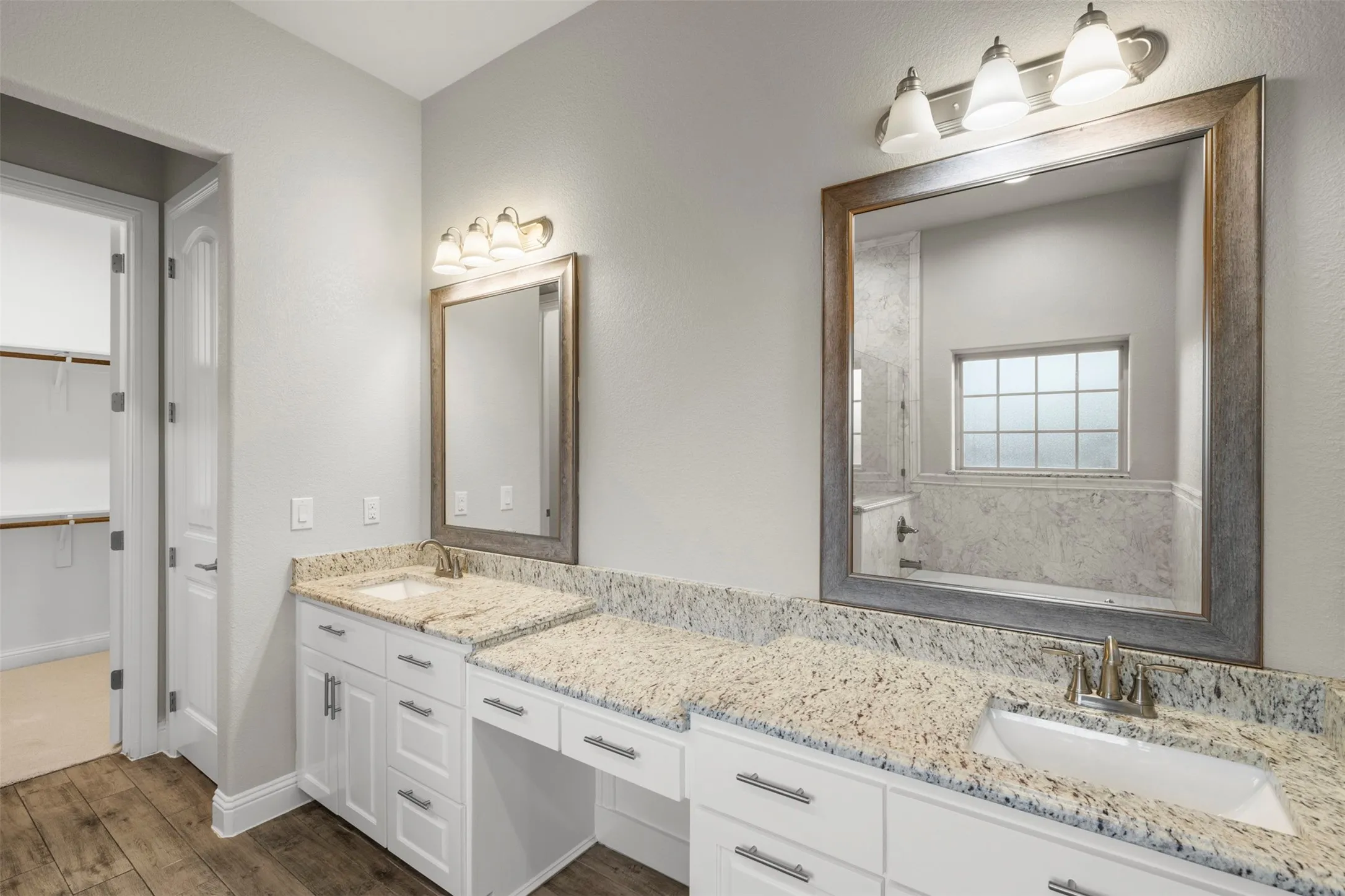 Dual vanity with granite countertops, undermount sinks, wood-finish flooring, and a walk-in closet