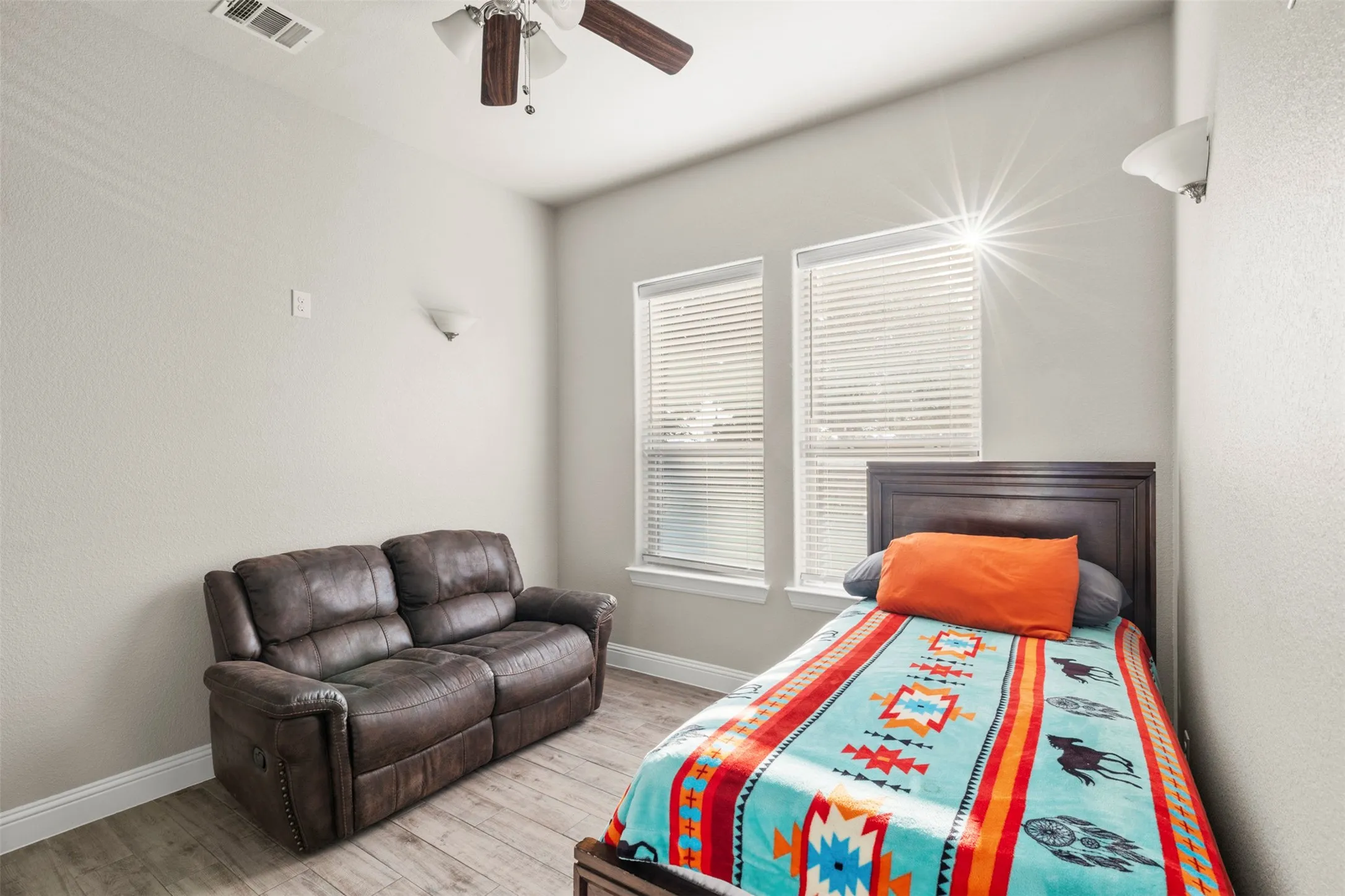 Vaulted ceiling with a ceiling fan, two windows with blinds, wood-finish flooring, and wall-mounted lighting