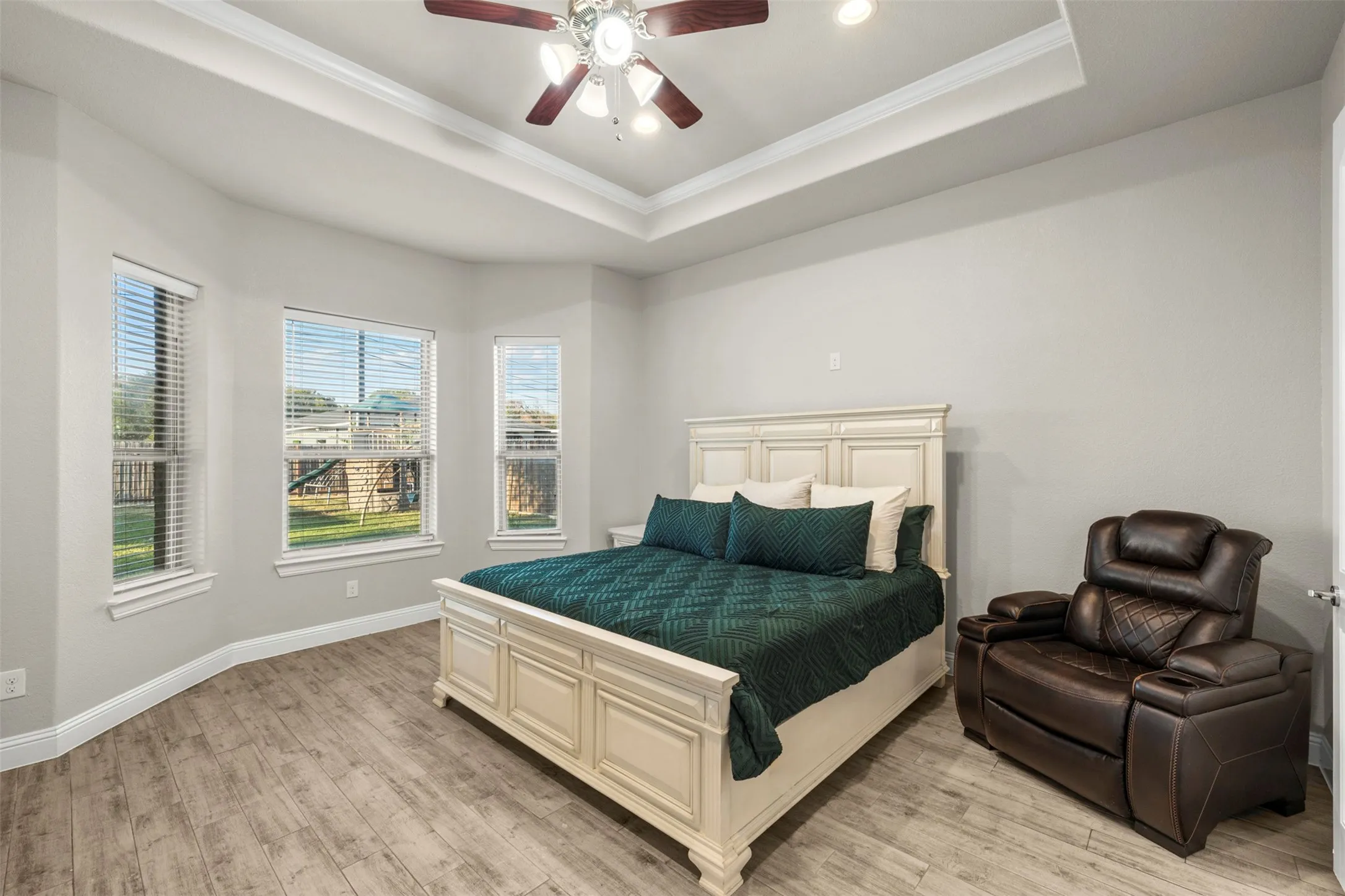 Tray ceiling with crown molding, wood-finish flooring, and a ceiling fan with integrated lighting