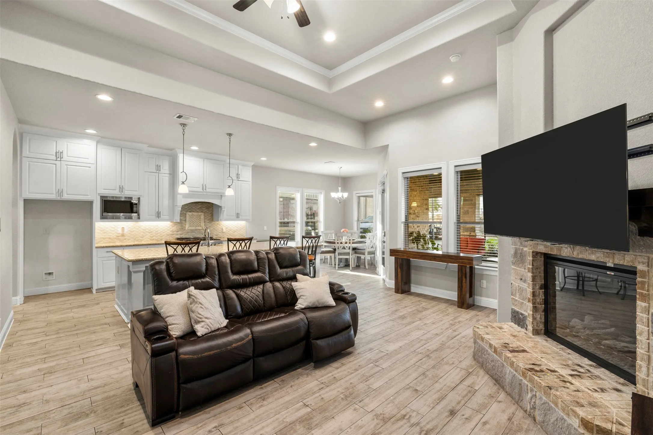 Open-concept living area featuring wood-finish flooring, a stone-surround fireplace with hearth, and recessed lighting