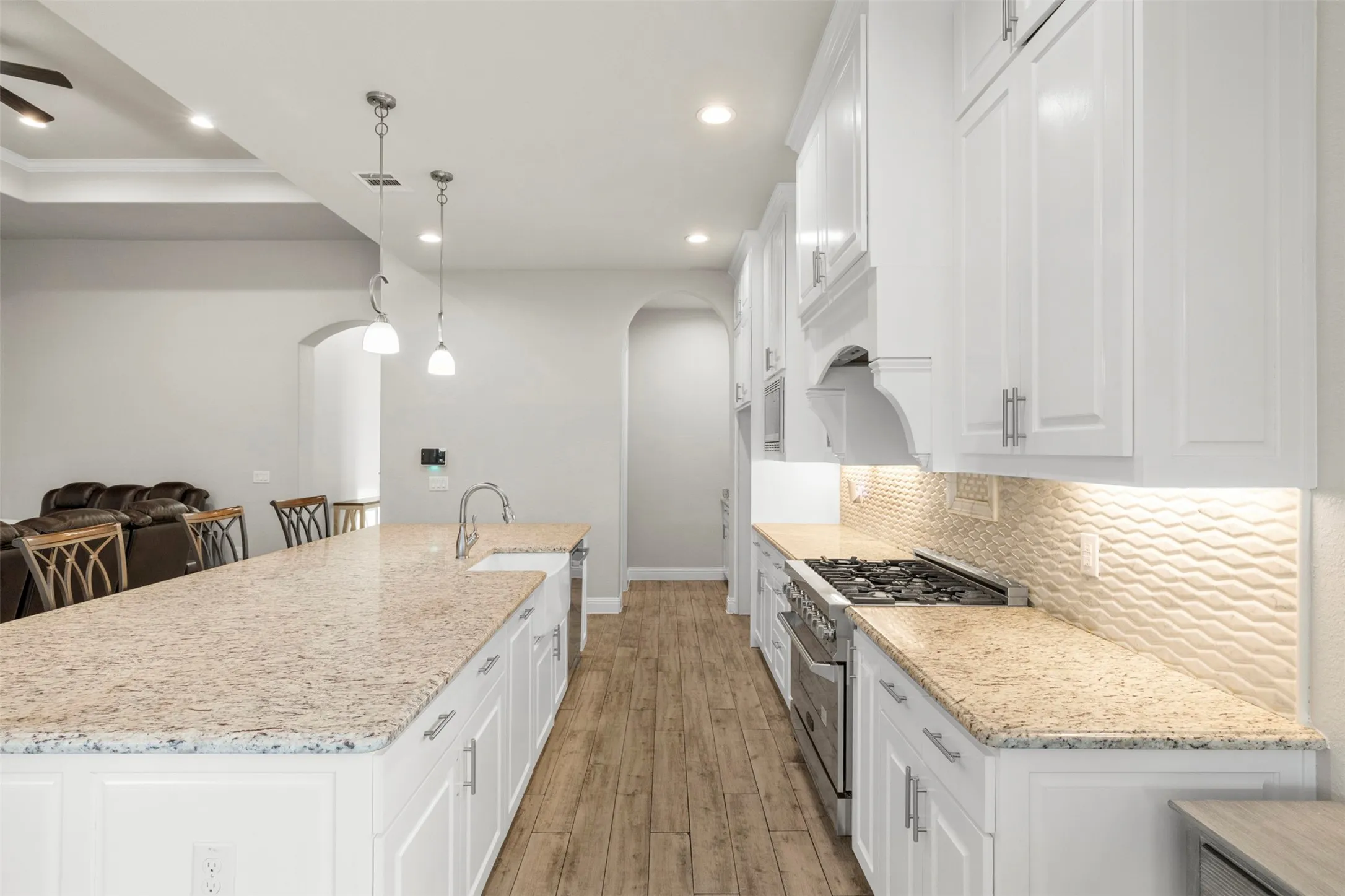 White cabinetry with recessed panel doors, light-toned countertops, wood-finish flooring, a stainless steel gas range, and a textured tile backsplash