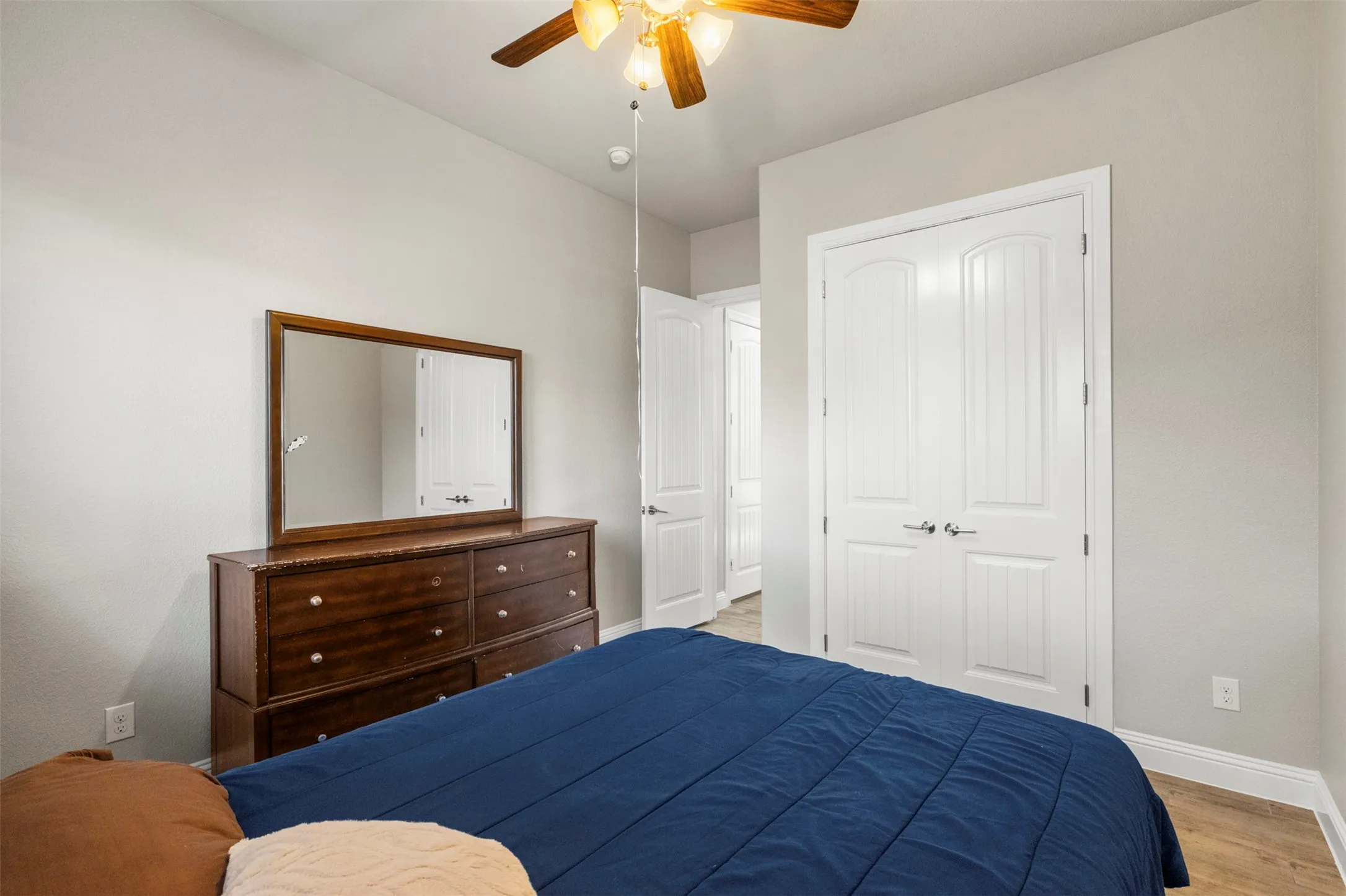 Ceiling fan with light fixture, light gray wall paint, white trim, white paneled doors, and wood-finish flooring
