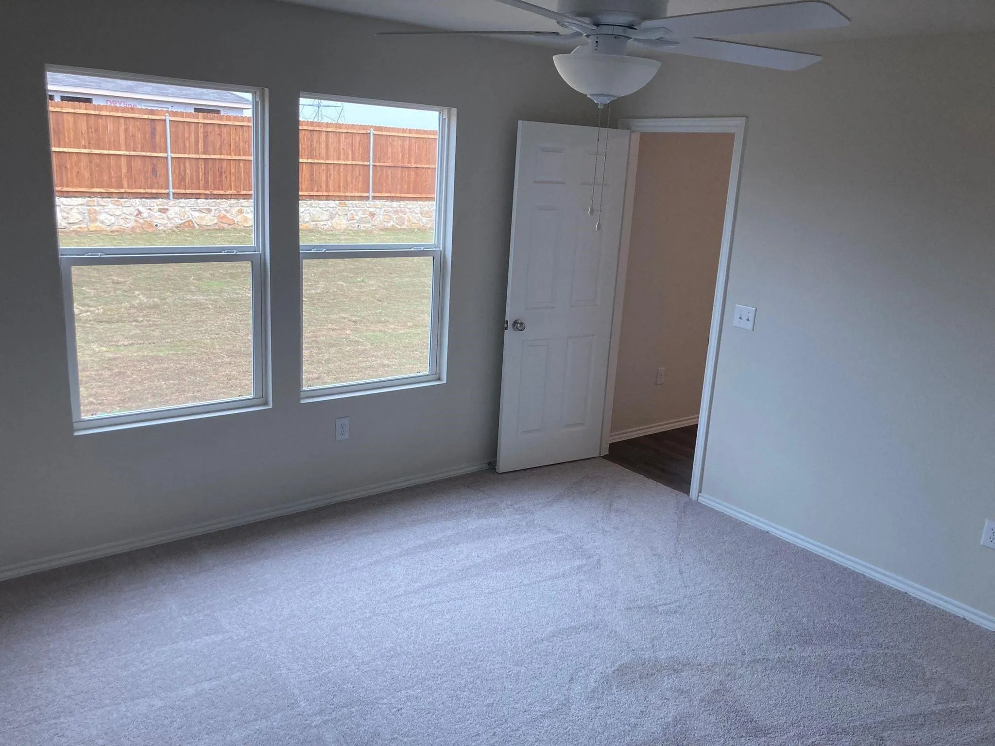Carpeted room with neutral wall tones, dual windows, and a ceiling fan