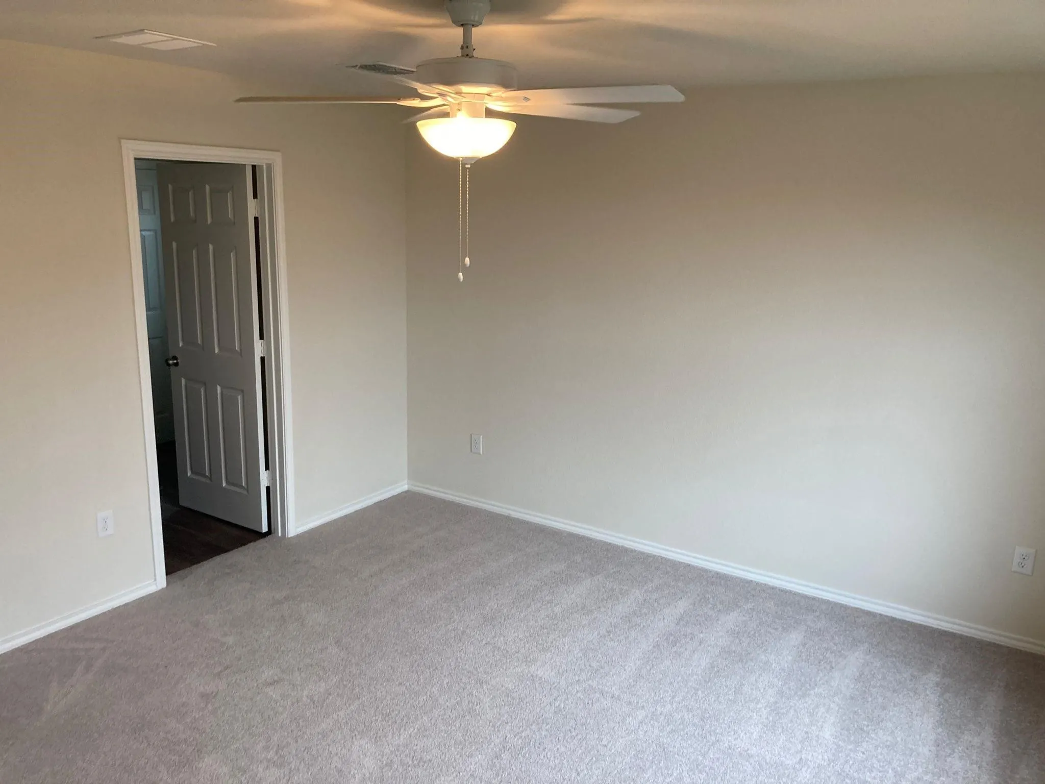 Neutral tone wall paint, light-toned carpeting, ceiling fan with integrated lighting, white trim, and a paneled interior door