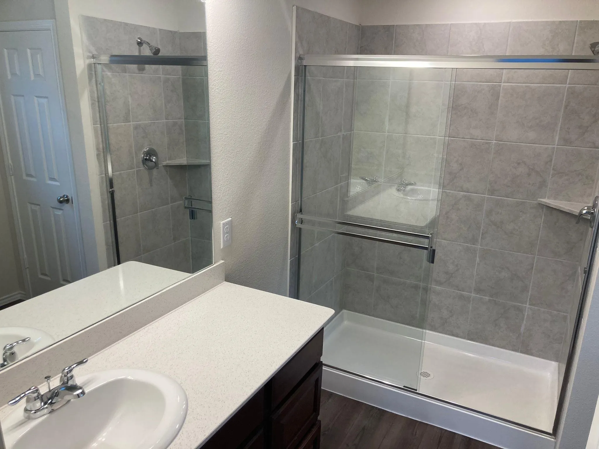 Shower with sliding glass enclosure, gray tile surround, and built-in corner shelf