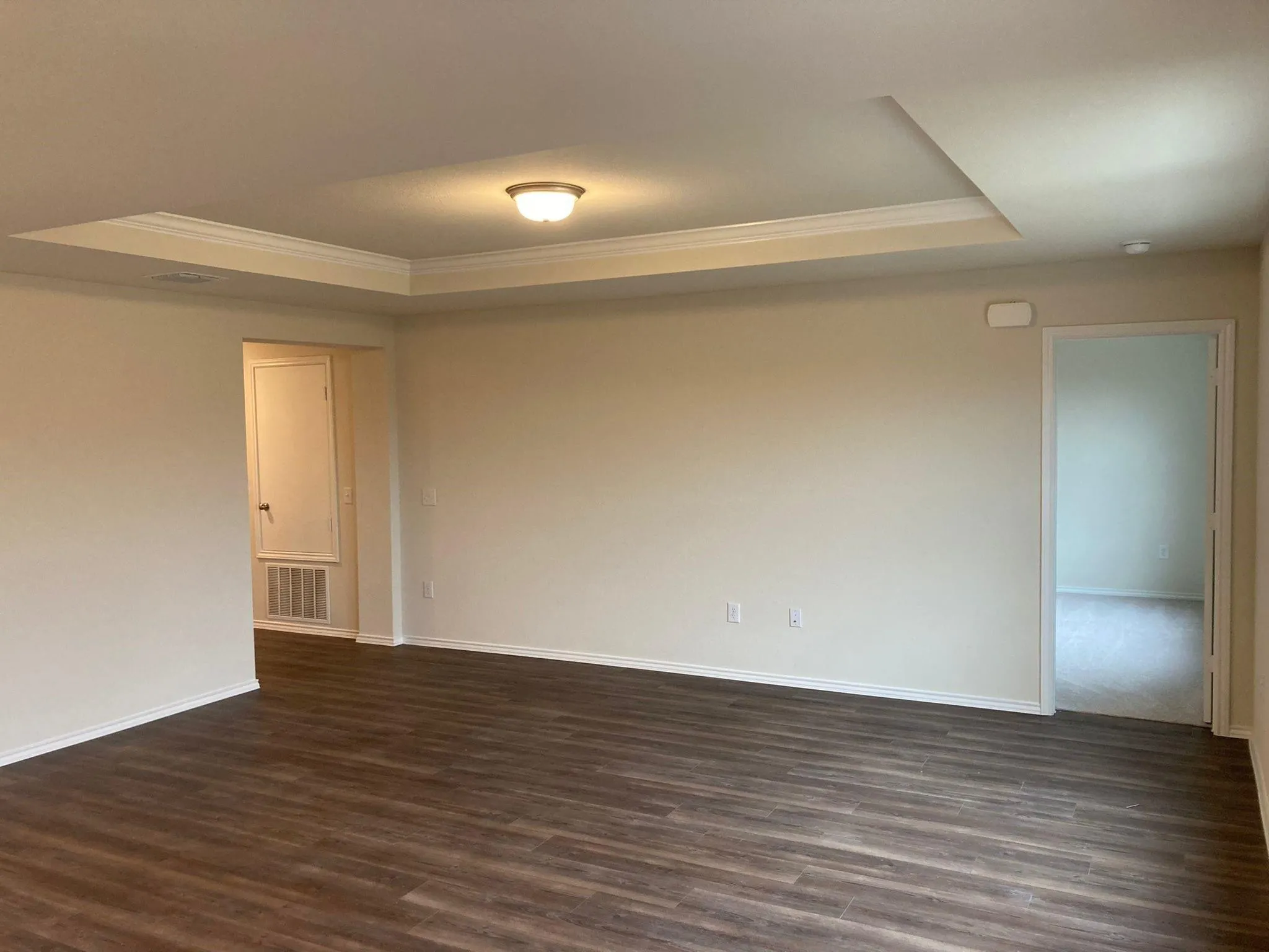 Tray ceiling with crown molding and flush mount lighting, wood-finish flooring, and neutral wall tones