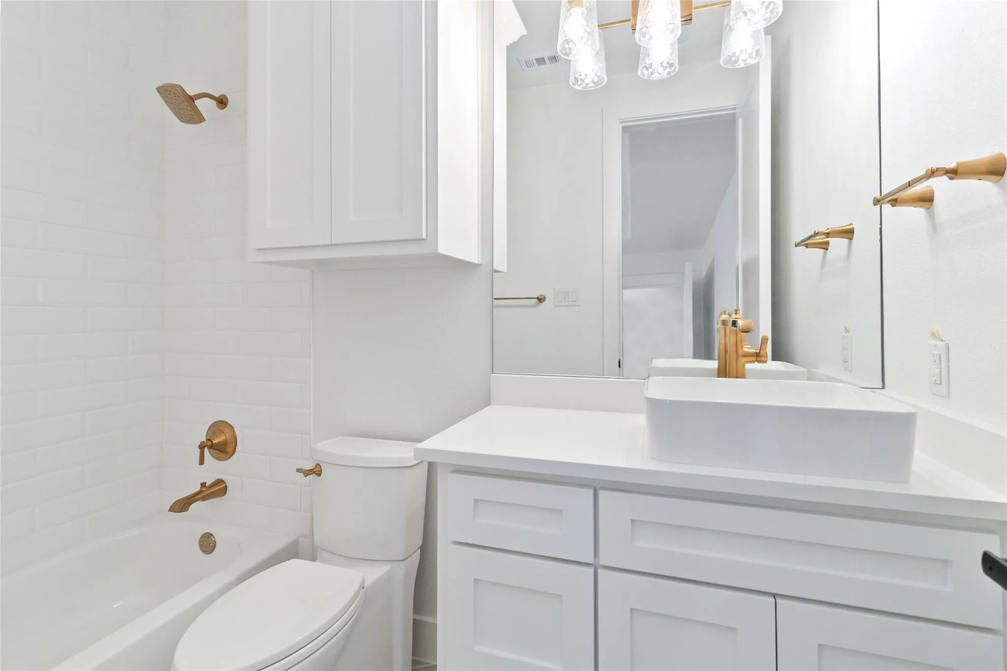 White subway tile shower surround, freestanding vanity with Shaker-style cabinetry, vessel sink, and gold-finish fixtures