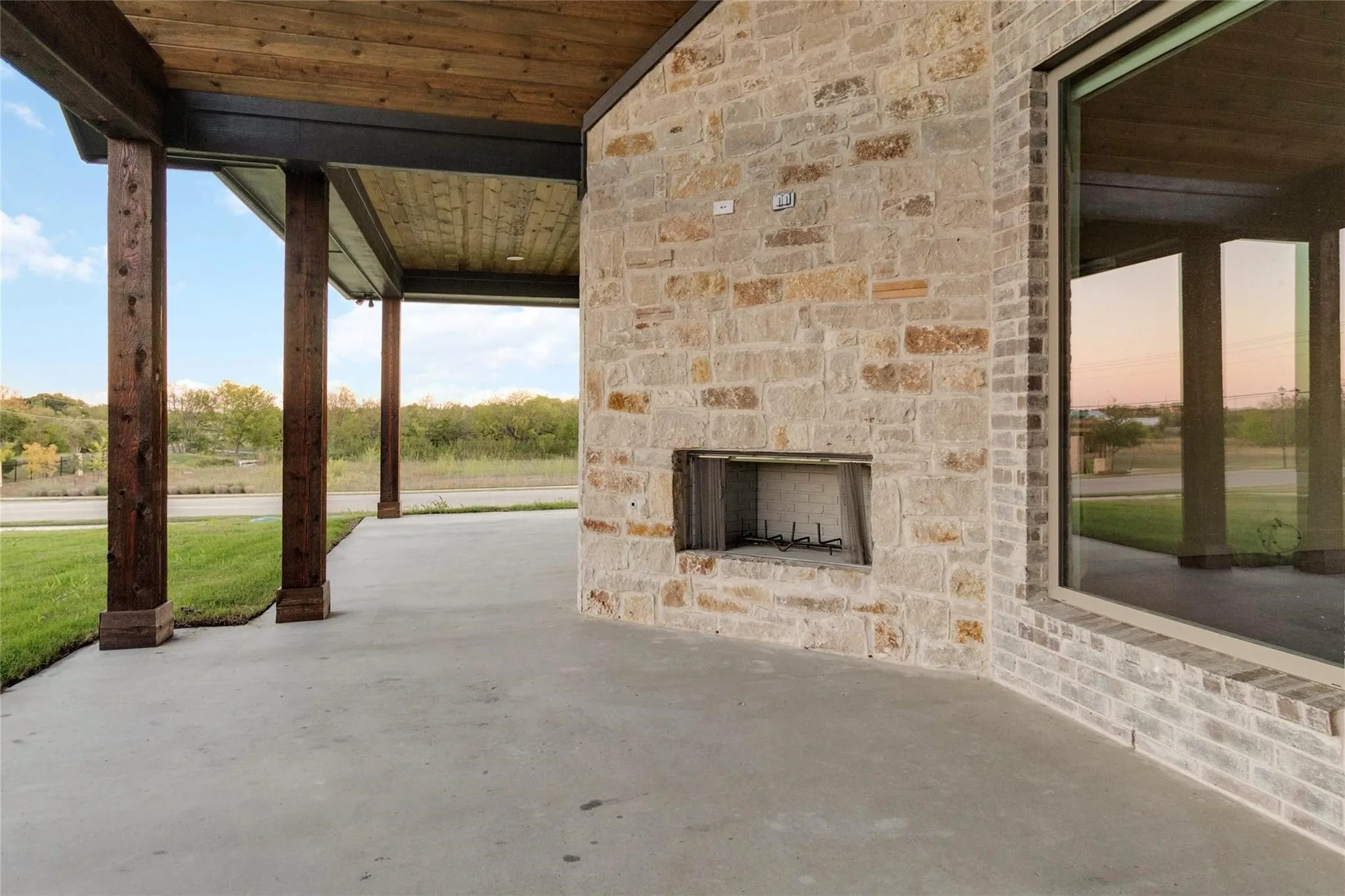 Expansive covered patio featuring a built-in stone fireplace, concrete flooring, and a natural wood plank ceiling