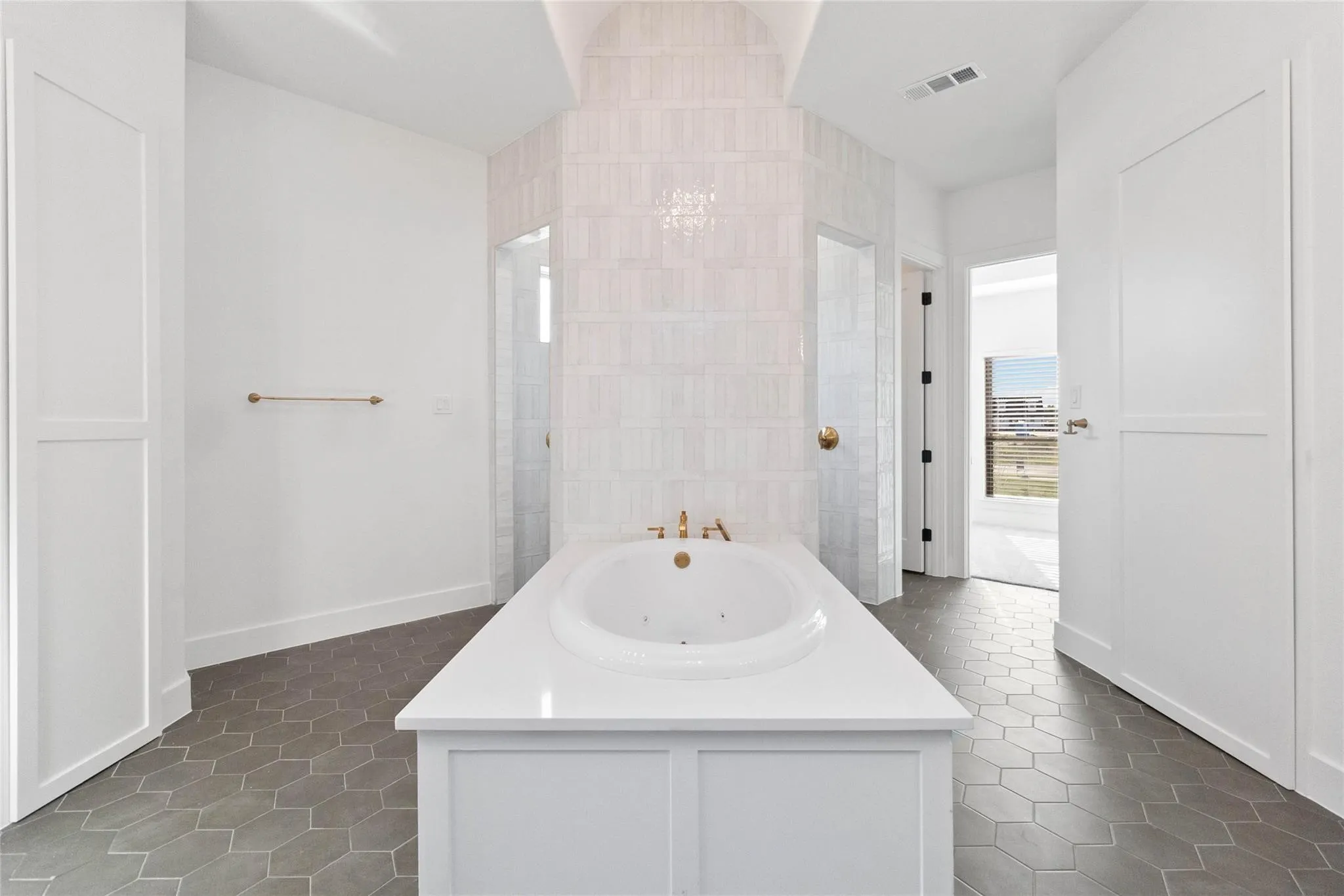 Freestanding soaking tub with gold-tone fixtures, surrounded by geometric tile flooring