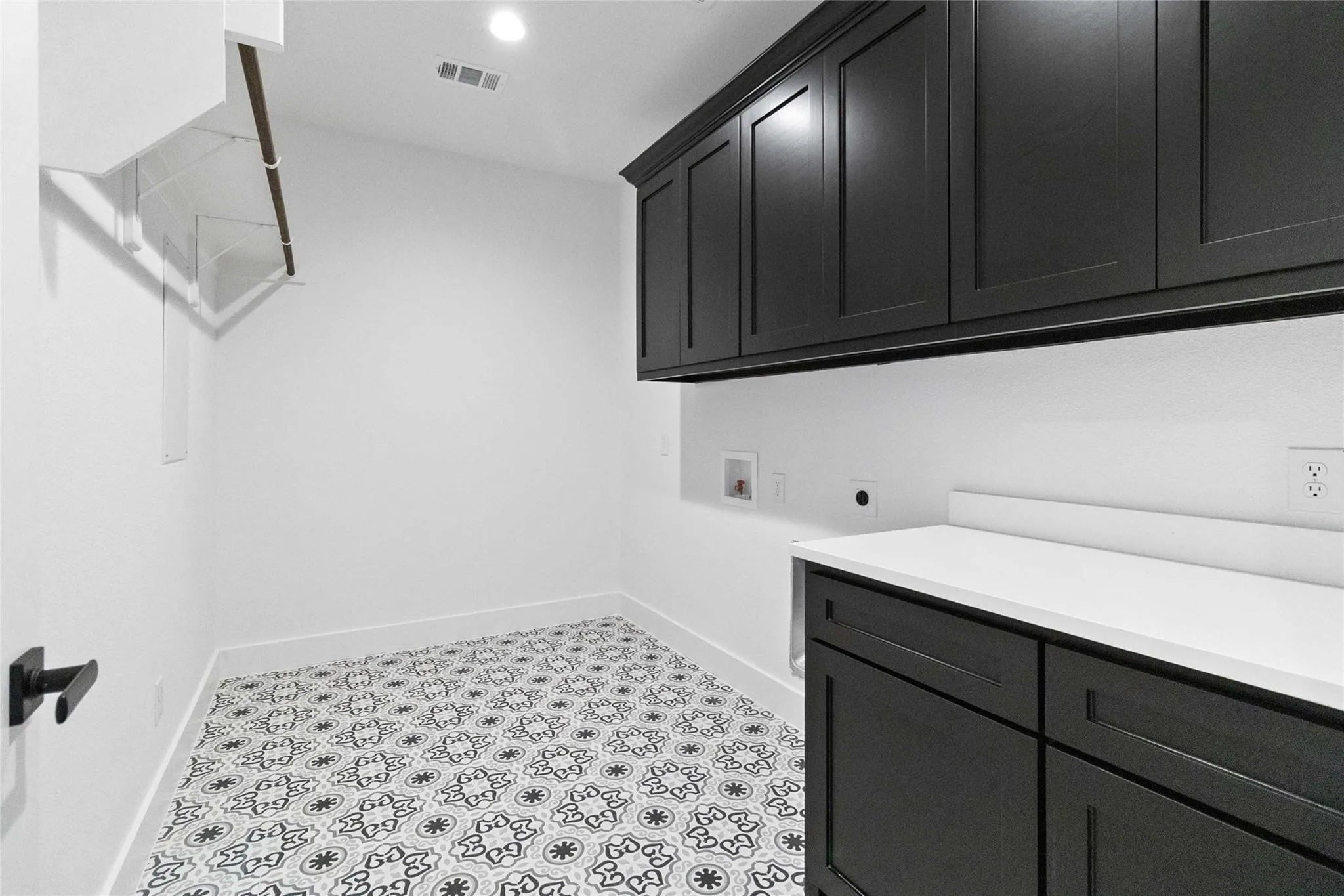 Laundry room featuring patterned floor tiles, dark cabinetry, a white countertop, and built-in shelving