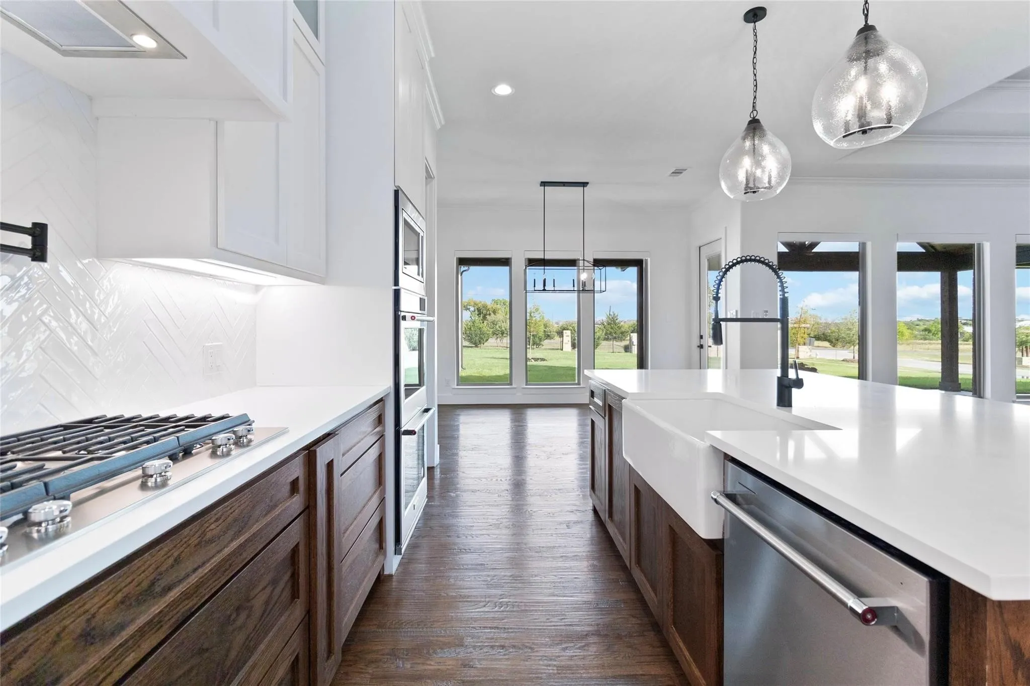 Kitchen featuring wood-finish flooring, white cabinetry, a built-in range, a large island with a farmhouse sink, and stainless steel appliances