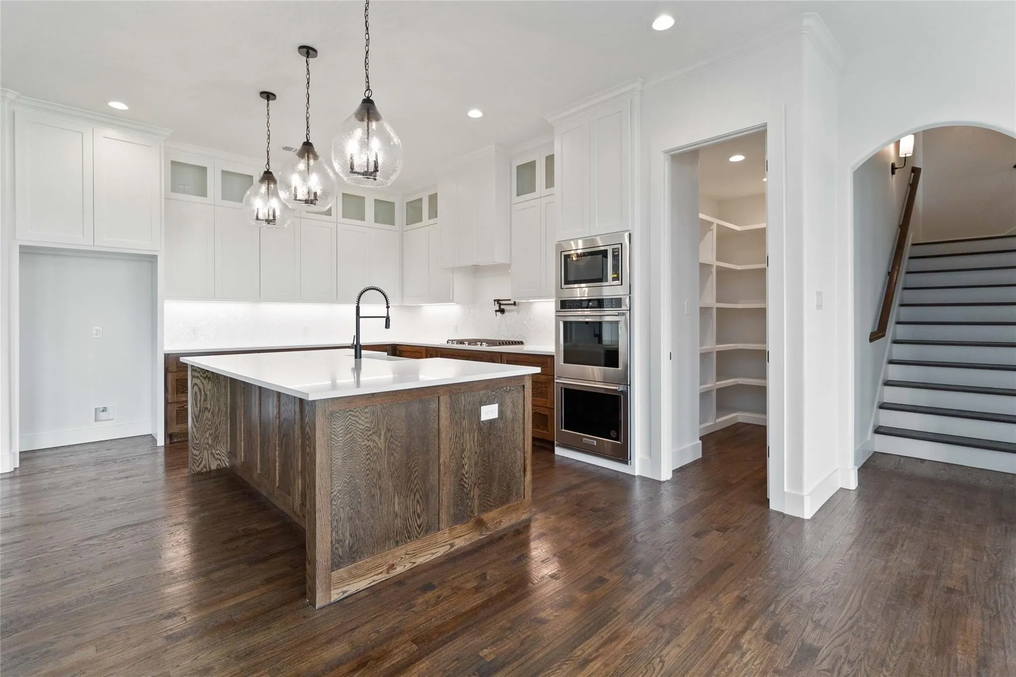 Kitchen with a wood-finish island, white cabinetry, integrated stainless steel appliances, and a walk-in pantry