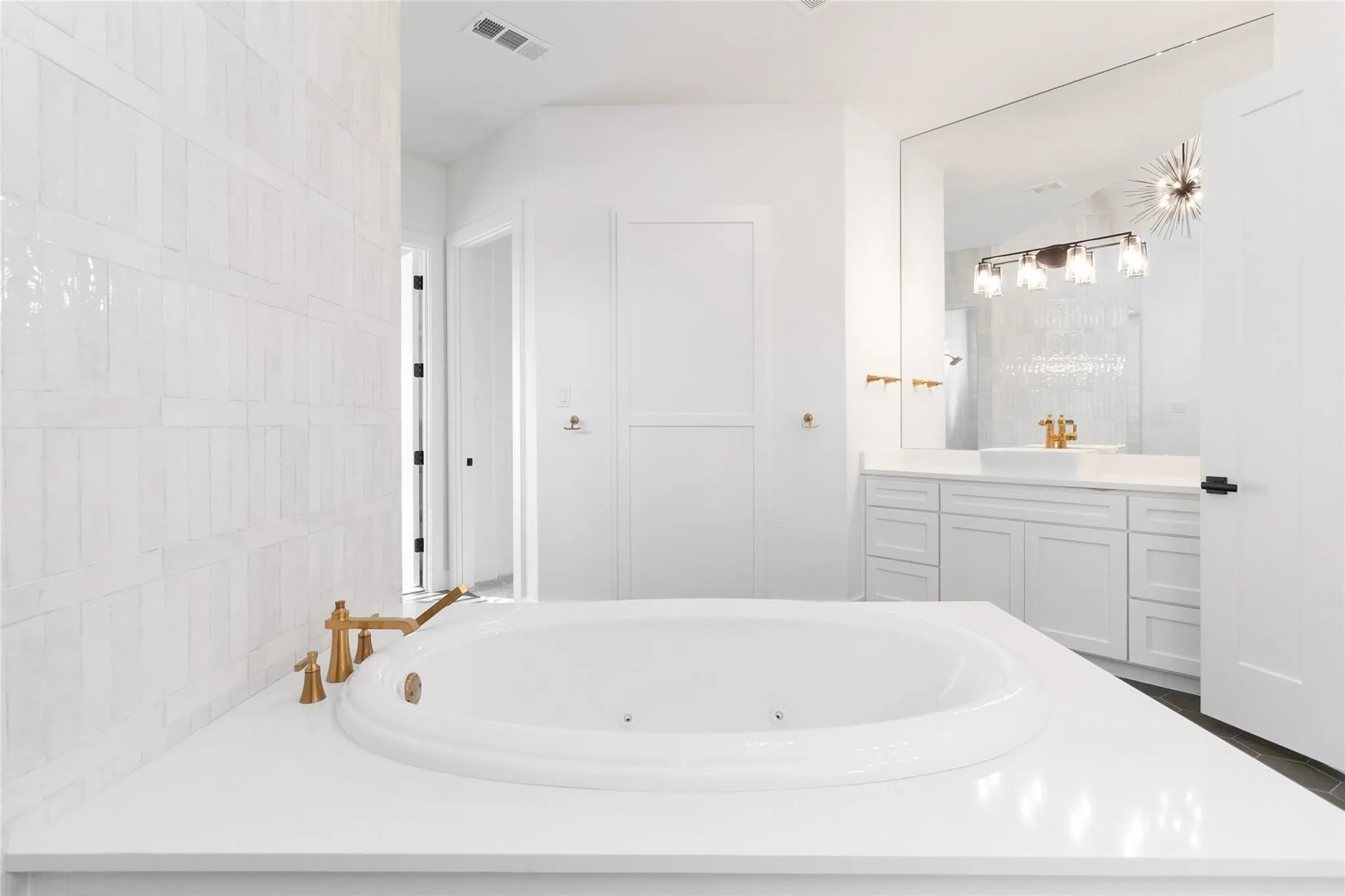 Soaking tub with brass-finish fixtures, white countertop, white cabinetry with integrated sinks, and patterned wall tile