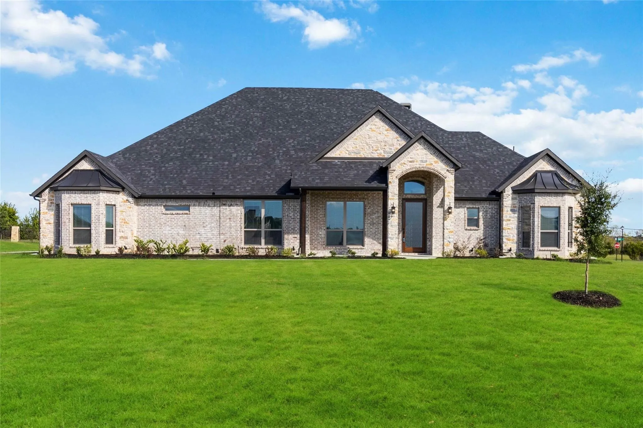 Brick and stone facade, dark shingle roof, arched entry, bay window, and a well-maintained lawn