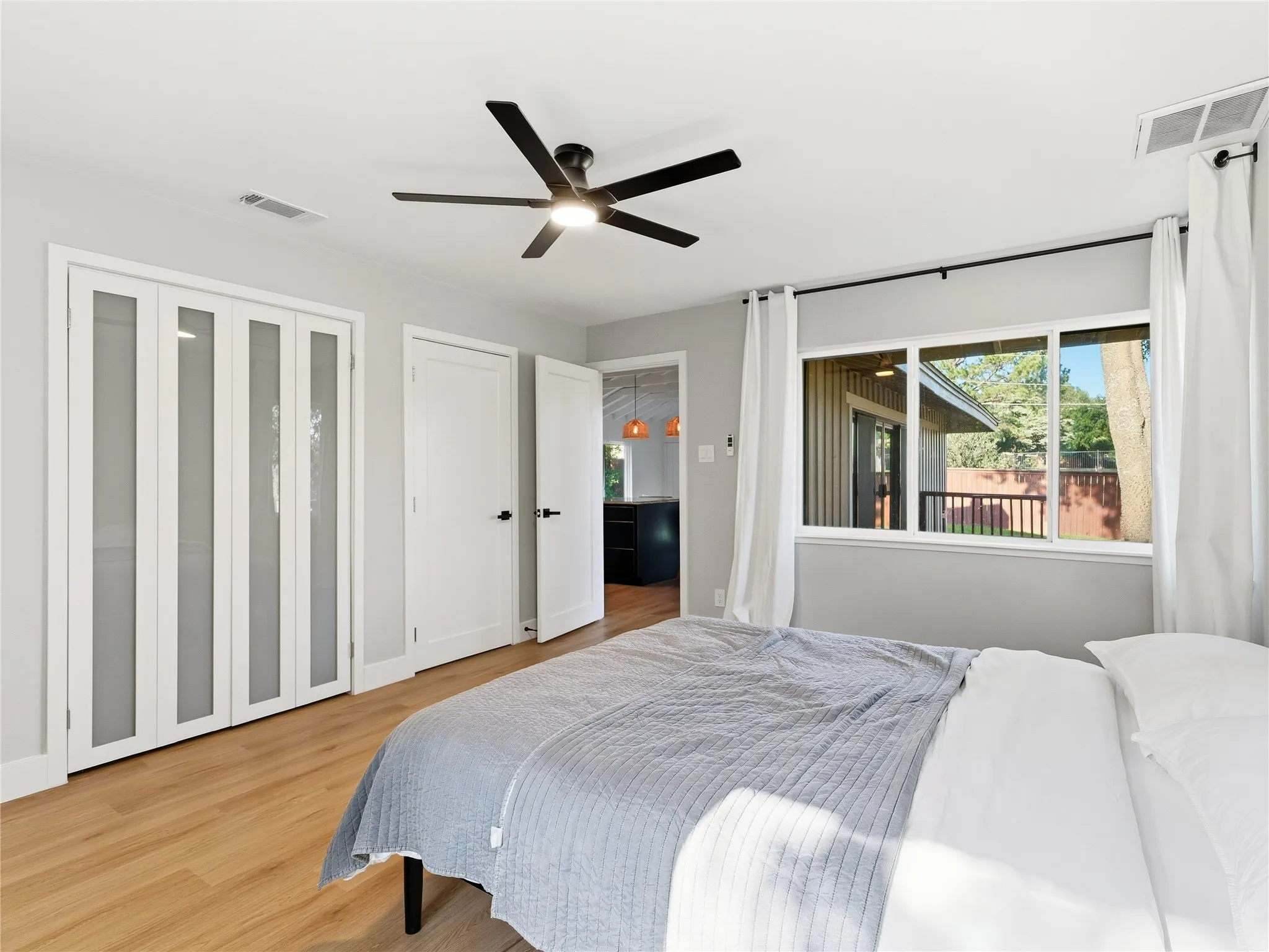Light wood-finish flooring, white bifold doors with frosted glass panels, modern ceiling fan with integrated lighting, and a large window with white trim