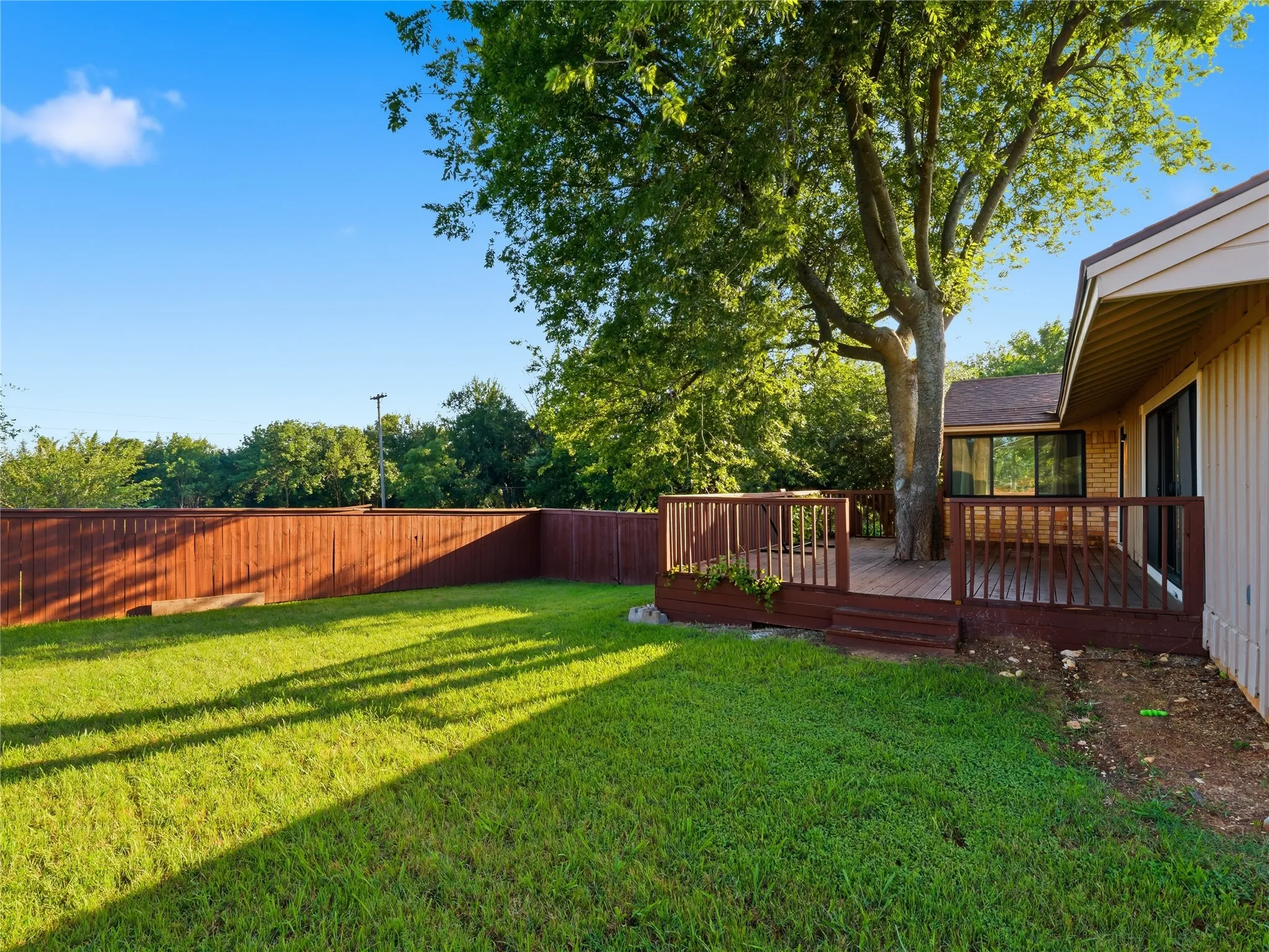 Expansive backyard featuring a manicured lawn, a stained wood privacy fence, and a multi-level wood deck