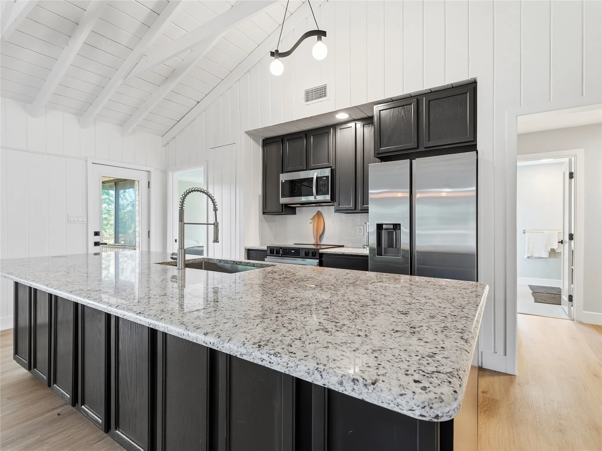 Vaulted ceiling with exposed beams, wood-finish flooring, and black cabinetry