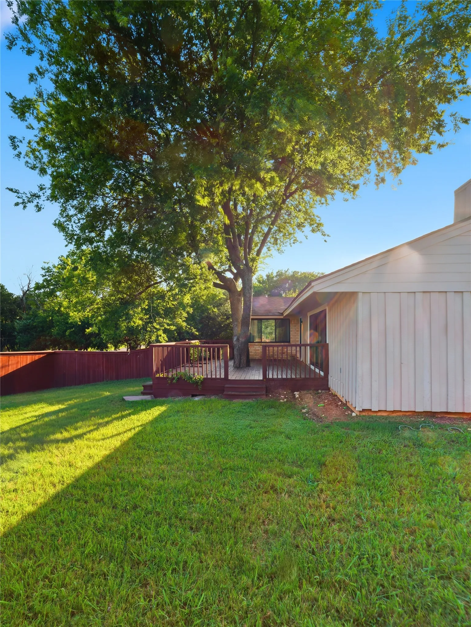 Expansive green lawn with a large, mature tree and a multi-level wood deck