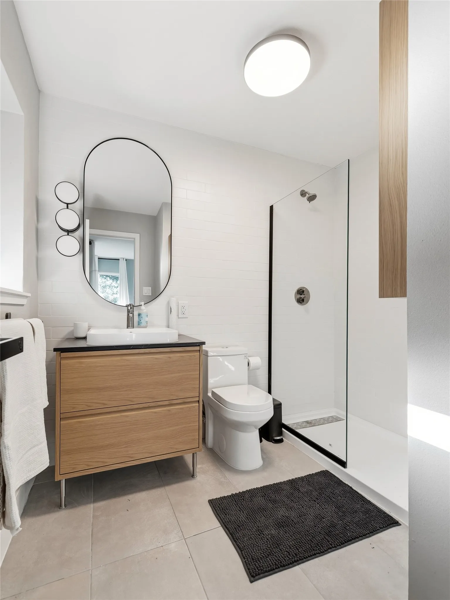 Tiled flooring, wood-finish vanity with a vessel sink, glass-enclosed shower, and subway tile walls