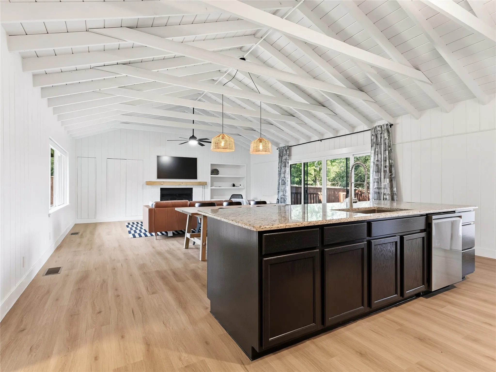 Vaulted ceiling with exposed beams, wood-finish flooring, kitchen island with granite countertop, built-in shelving, and sliding glass doors