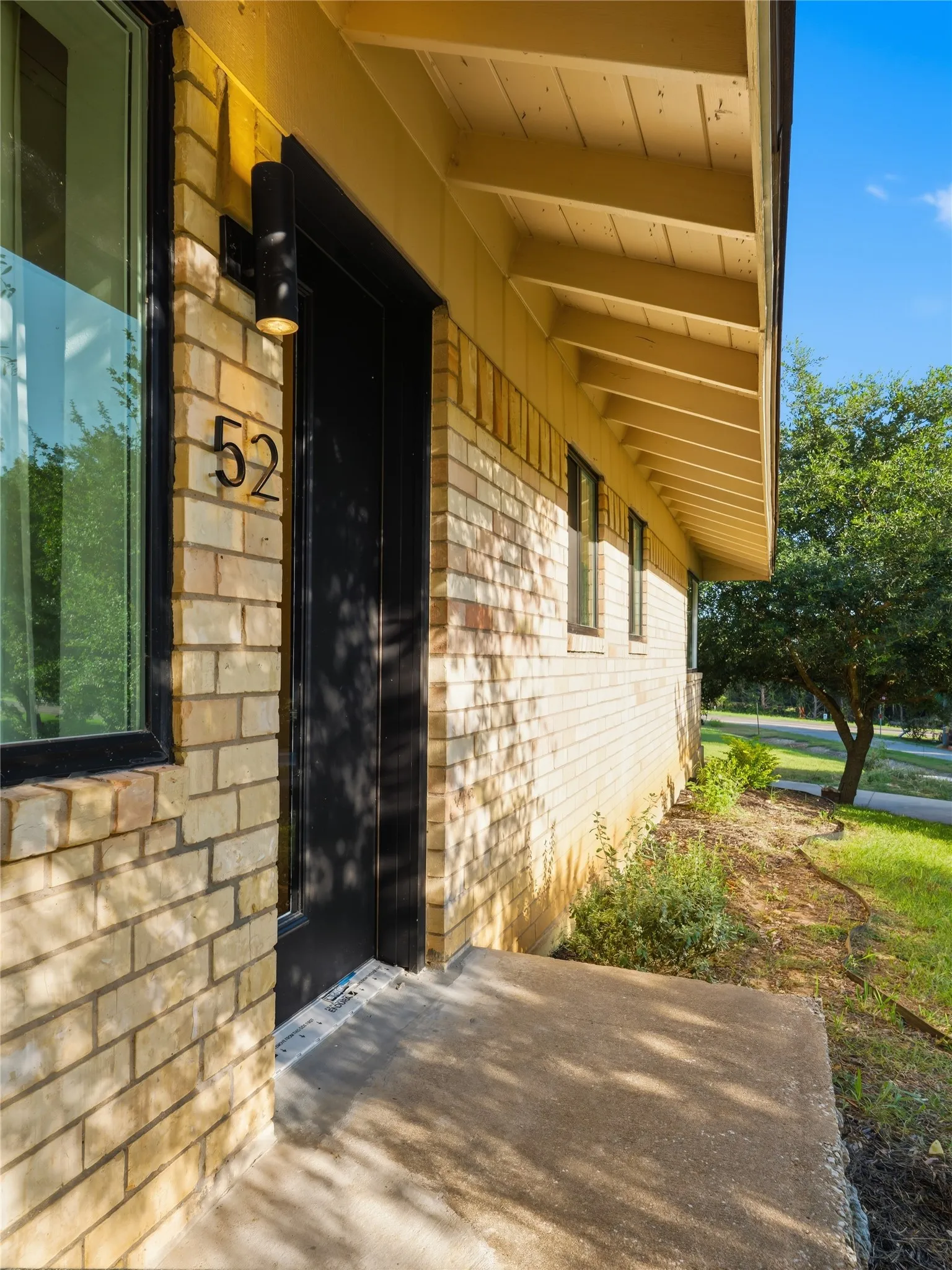 Brick exterior with a concrete entryway, black door, and exposed soffit rafter tails