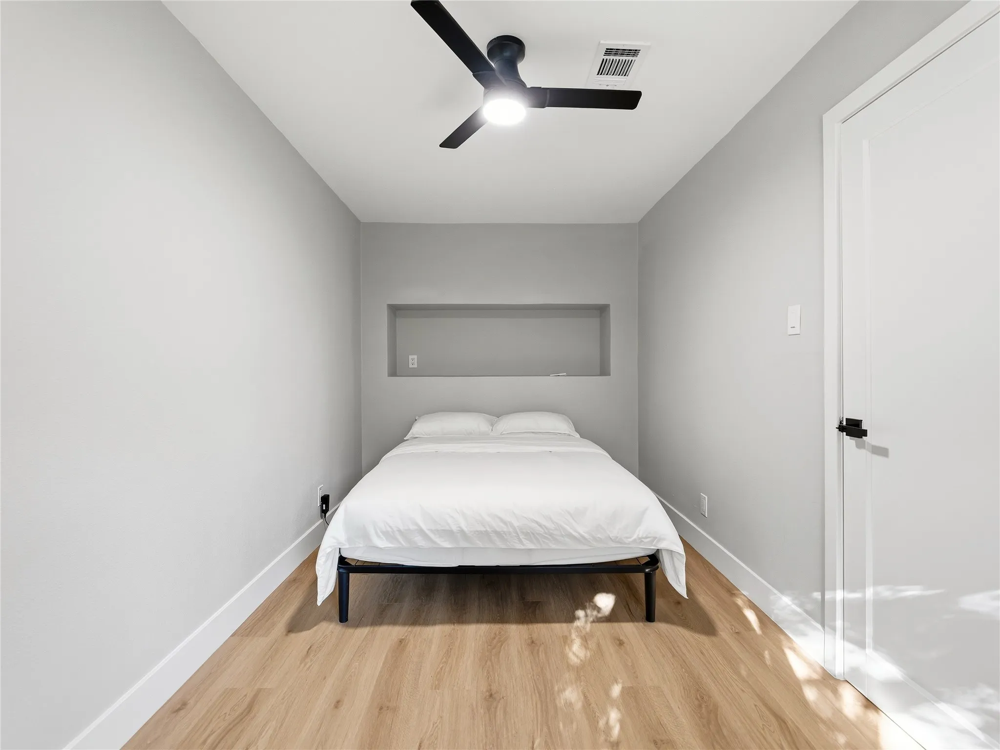 Recessed wall niche, contemporary ceiling fan, wood-finish flooring, white paneled door with matte black hardware, and bright interior lighting