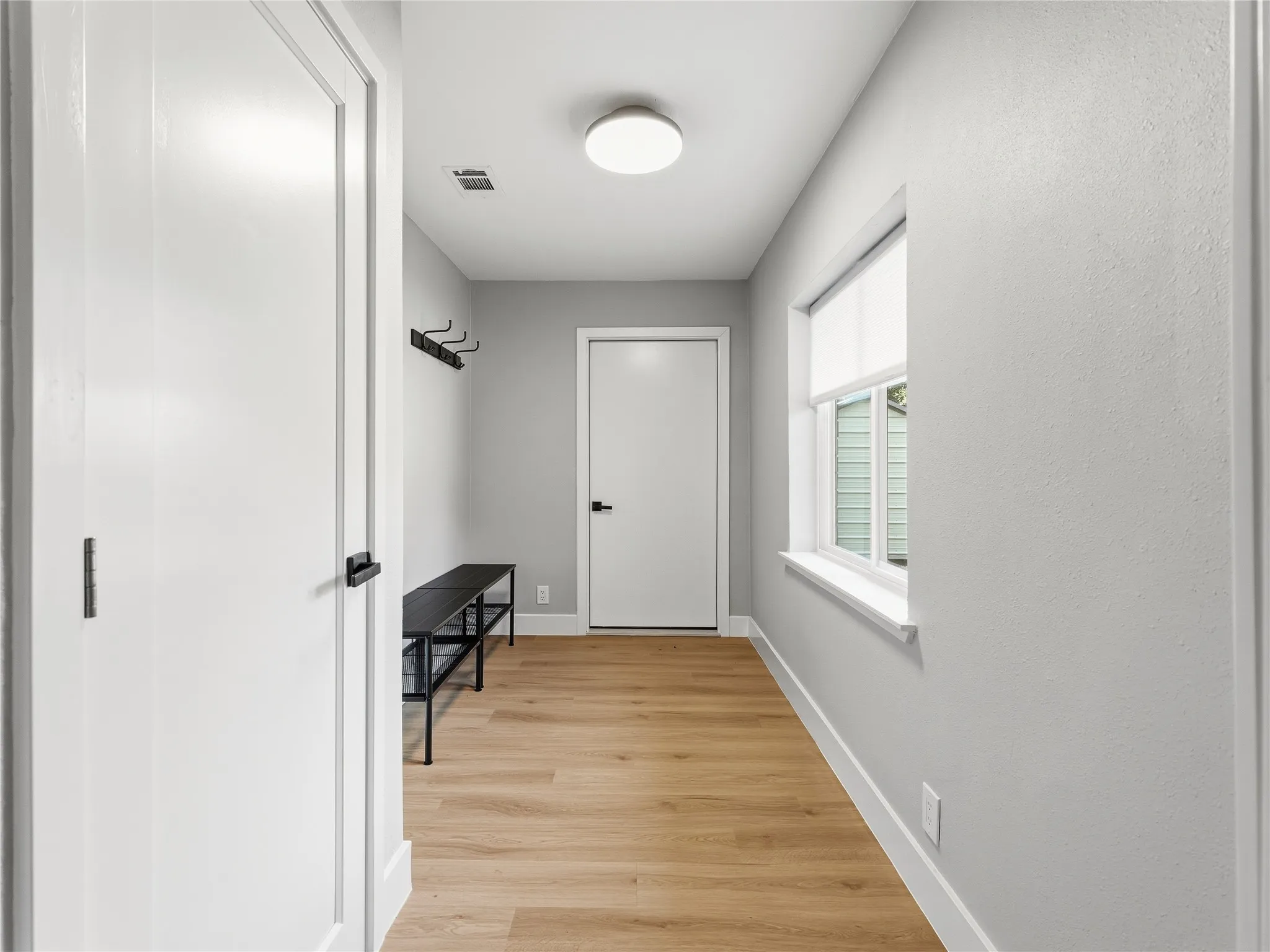 Hallway featuring wood-finish flooring, a flush-mount ceiling light, a window with a roller shade, and white trim throughout
