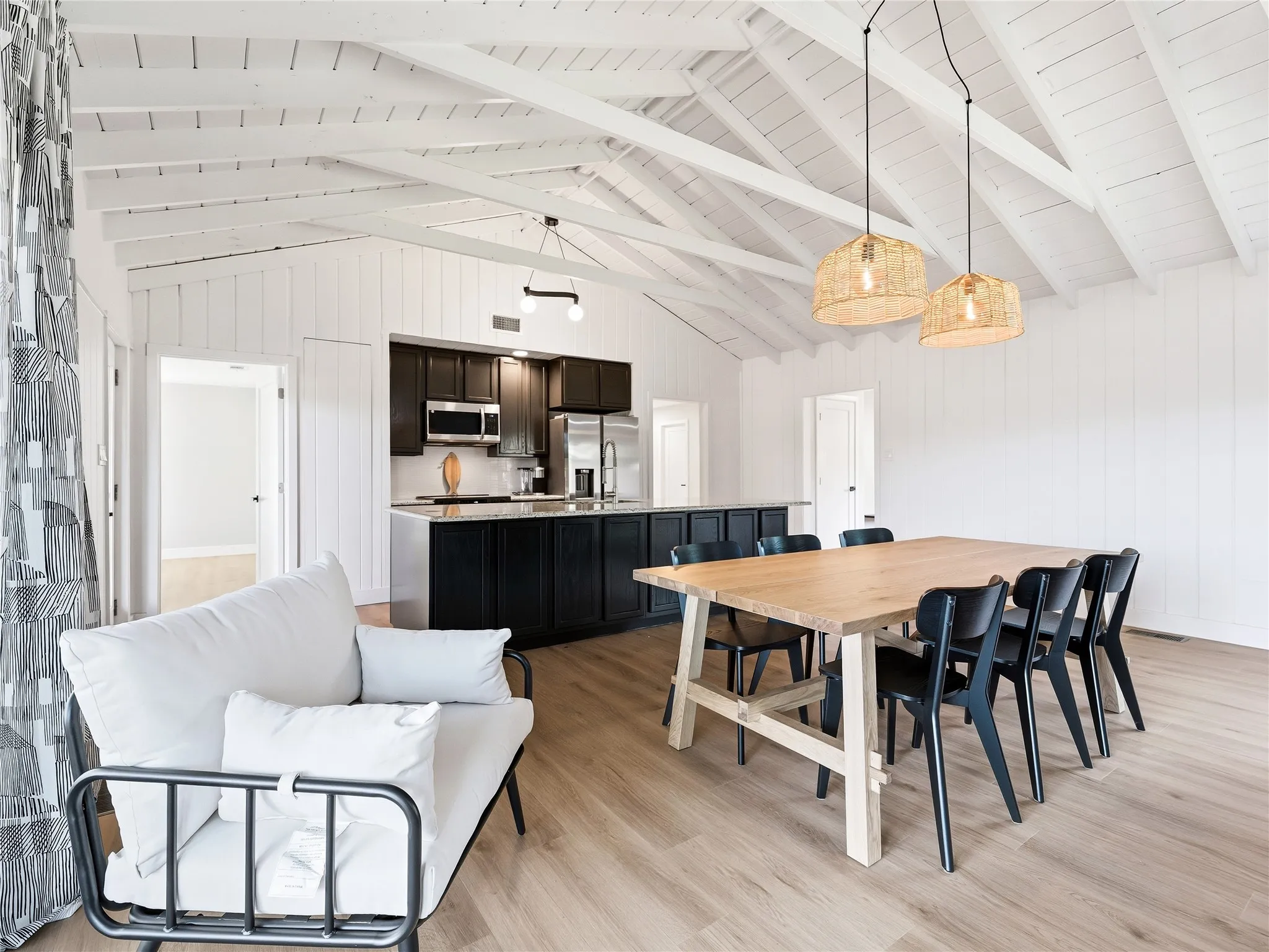 Vaulted ceiling with exposed beams, wood-finish flooring, recessed lighting, and kitchen with dark cabinetry and stainless steel appliances