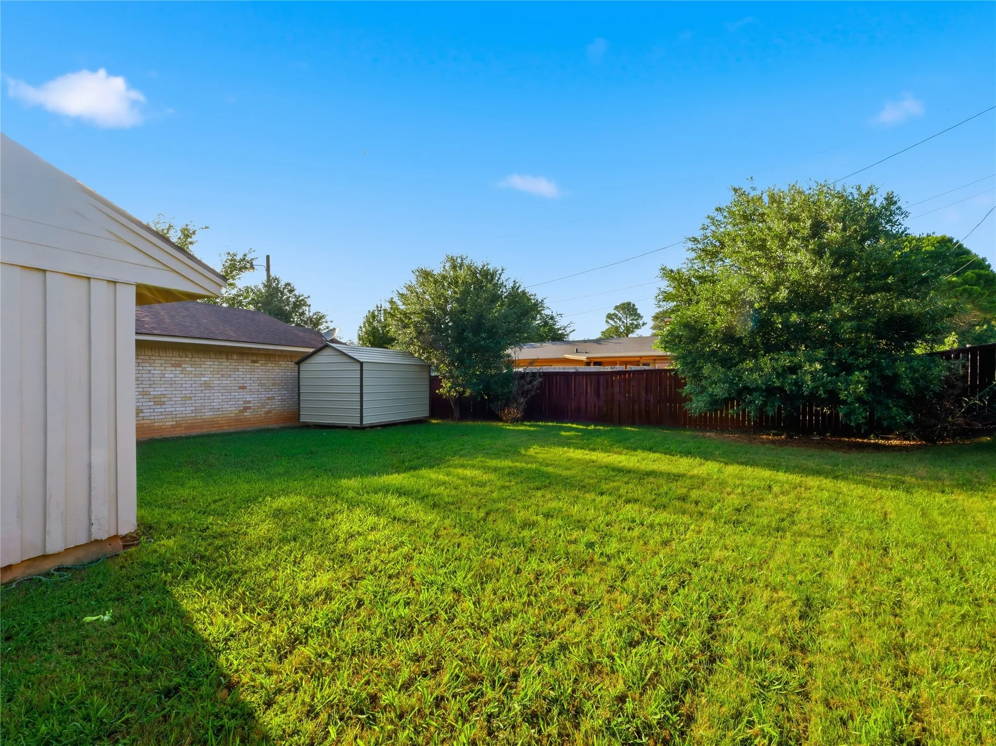 Expansive lawn space featuring a storage shed and mature trees, enclosed by a wooden privacy fence