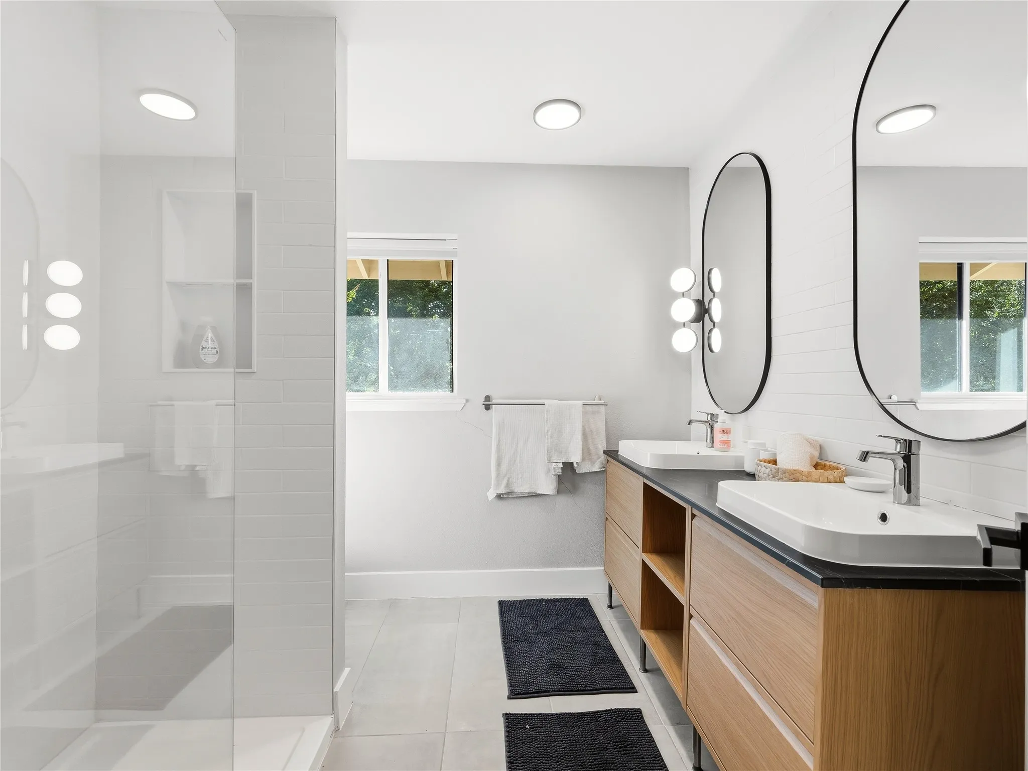 Dual wood-finish vanities with vessel sinks, black countertops, and oval mirrors