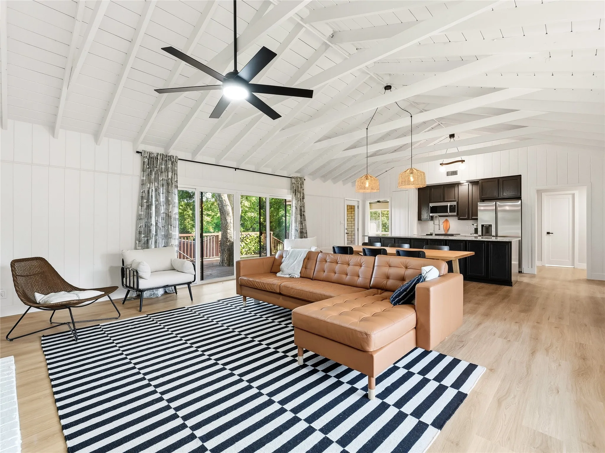 White vaulted ceiling with exposed beams, wood-finish flooring, dark wood cabinetry, stainless steel appliances, and sliding glass doors