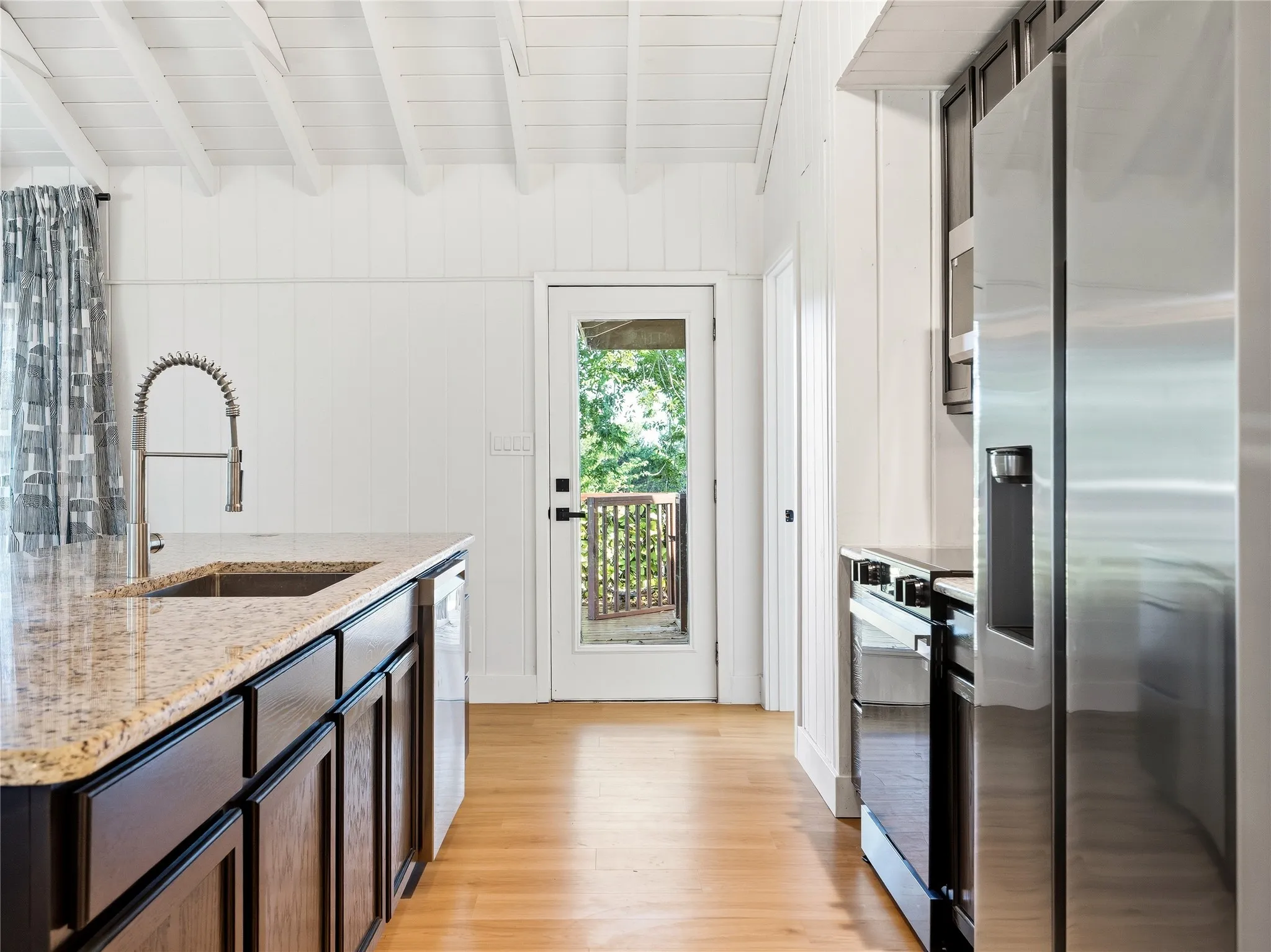 Kitchen featuring a granite countertop, stainless steel appliances, wood-finish flooring, and exposed white ceiling beams