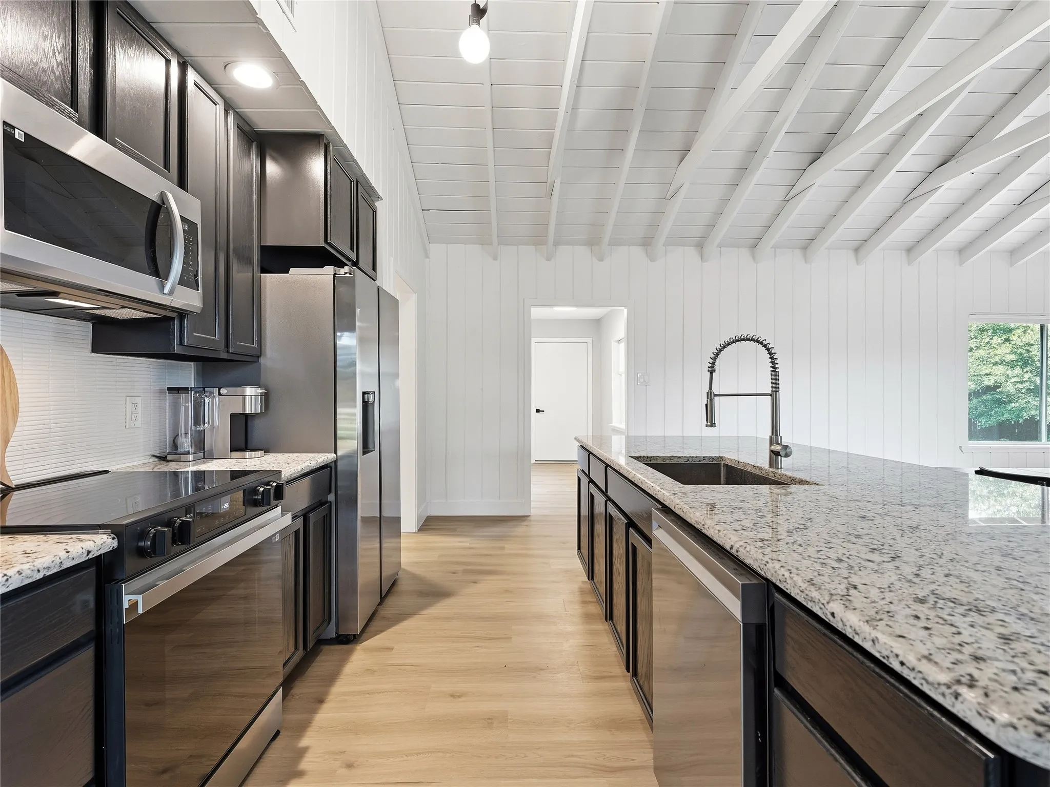 Kitchen featuring stainless steel appliances, dark wood cabinetry, light granite countertops, a built-in sink with a pull-down faucet, and wood-finish flooring