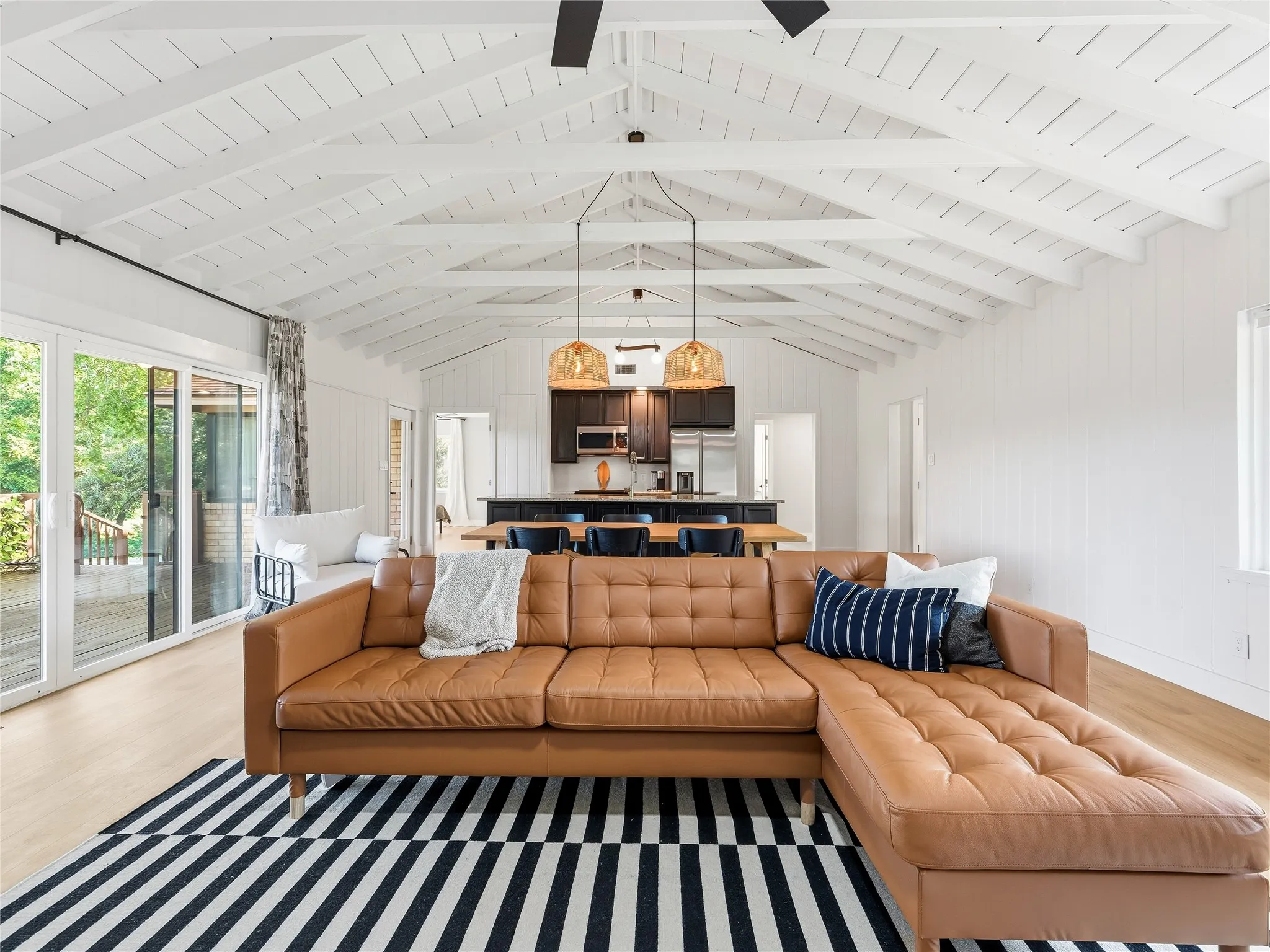 Vaulted plank ceilings, light wood-finish flooring, and sliding glass doors leading to an exterior deck