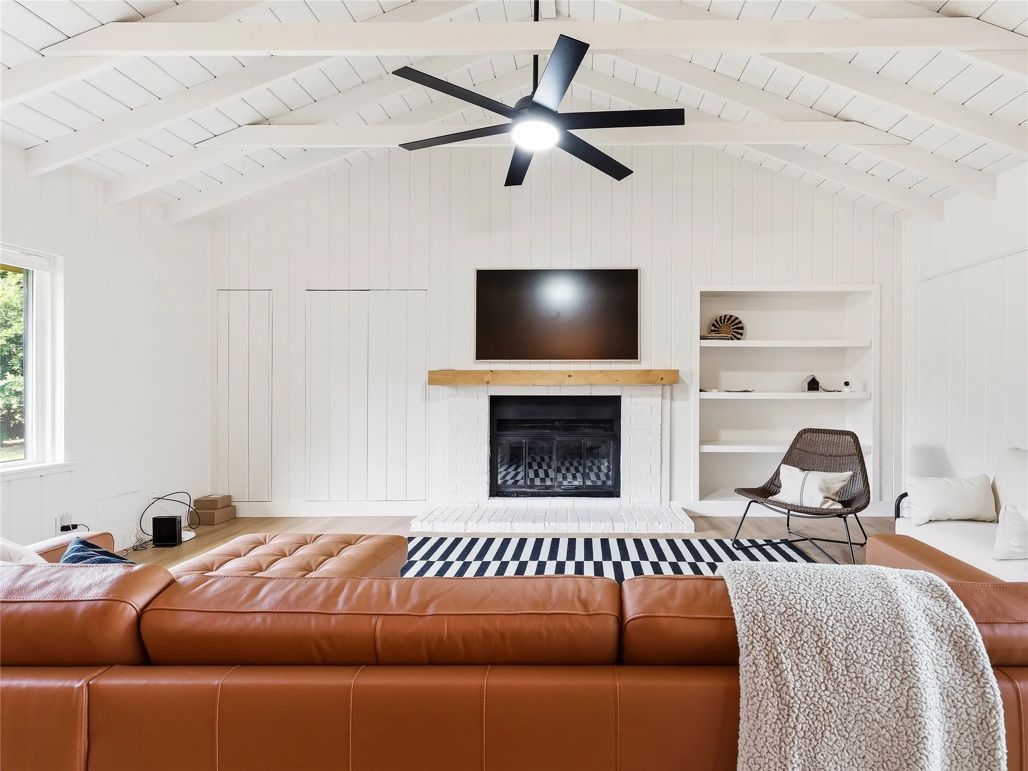 Vaulted ceiling with exposed beams, wood-finish flooring, white shiplap walls, built-in shelving, and a fireplace with a wood mantle