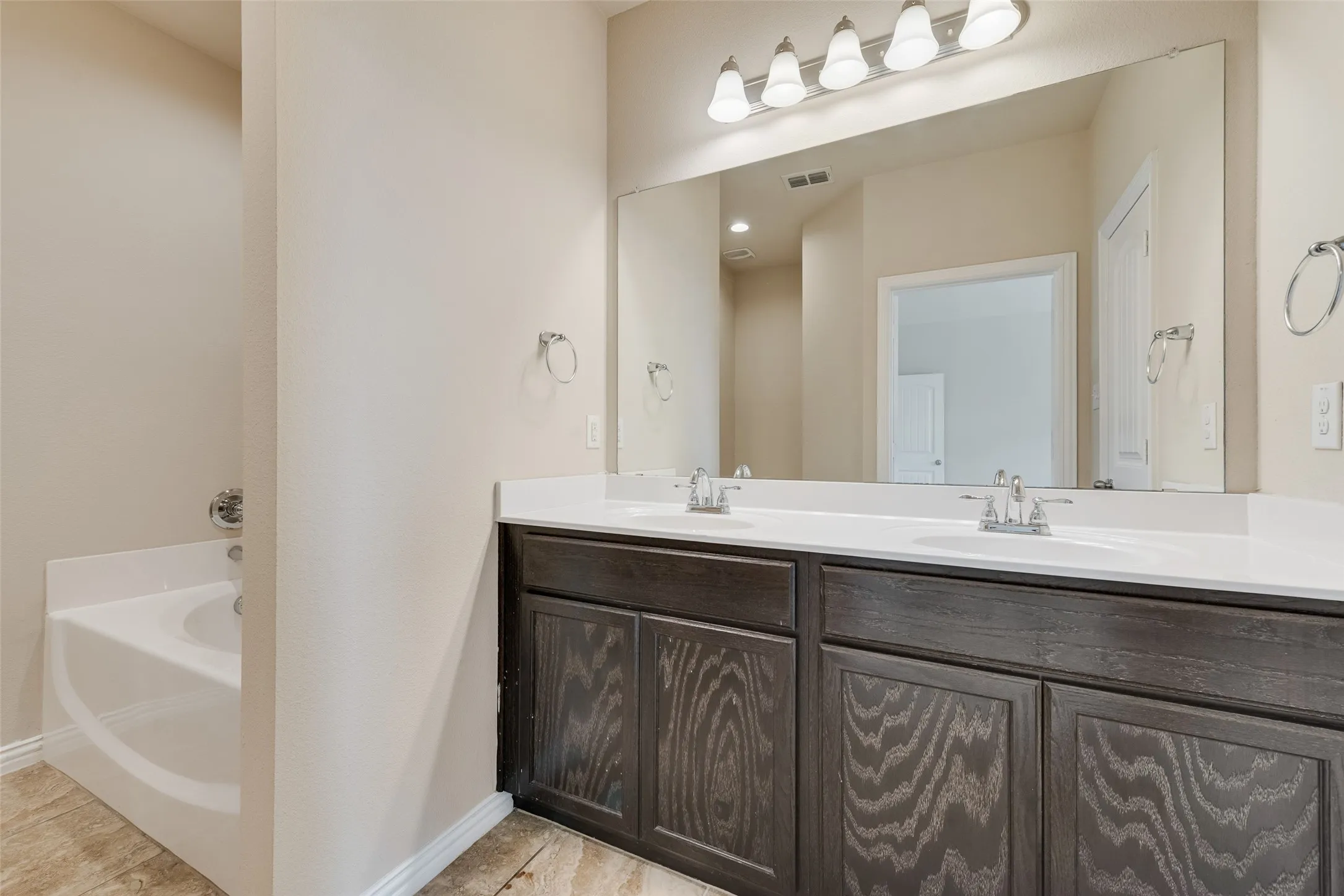 Dual basin vanity with white countertops, dark wood-finish cabinetry, and a full-width mirror
